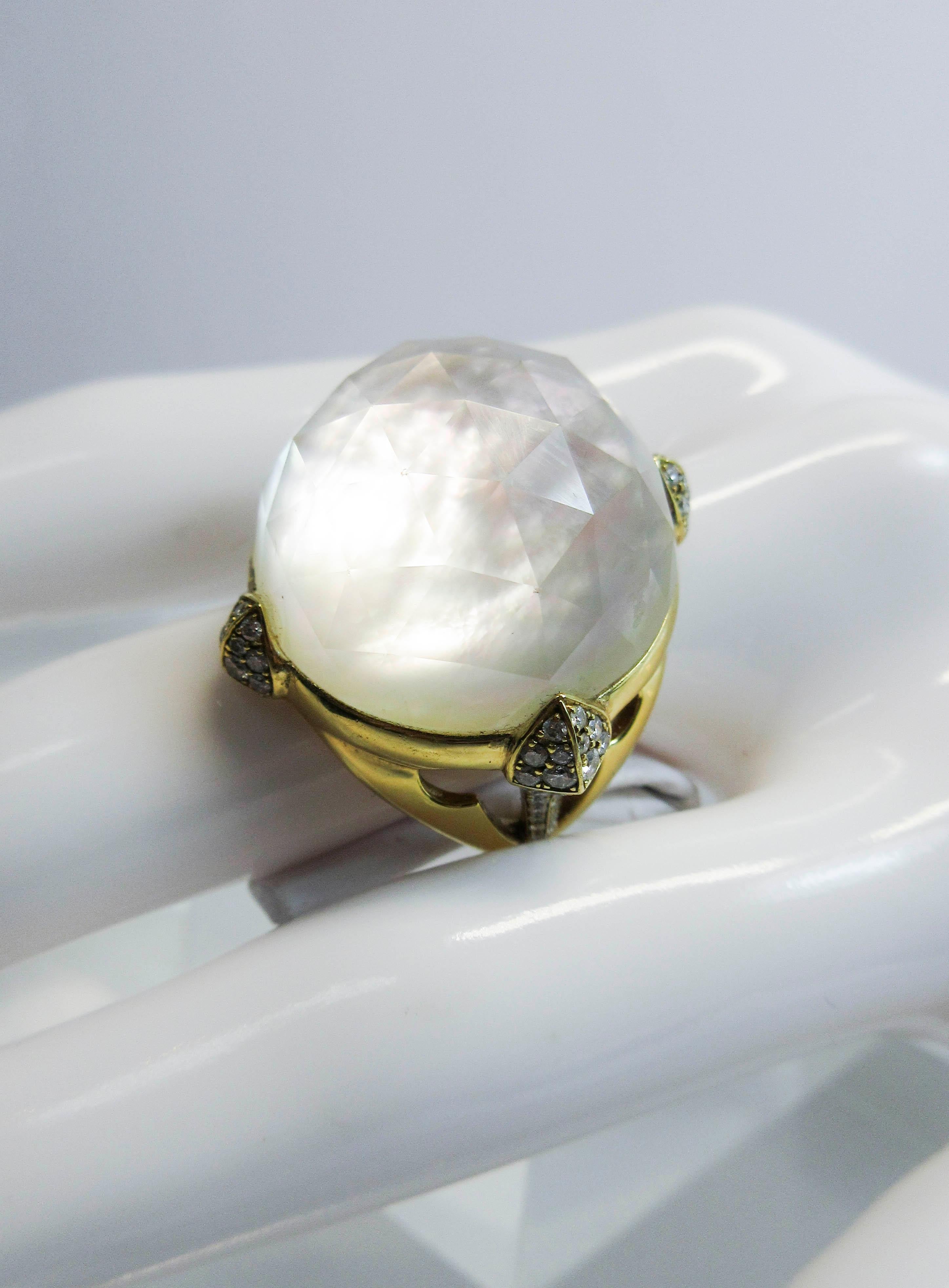 This is a stunning Stephen Webster design. The ring is composed of 18kt yellow gold with side diamond accents, and a center stone of faceted quartz with a mother of pearl base. An absolutely captivating cocktail ring. Size 7. Measures approximately