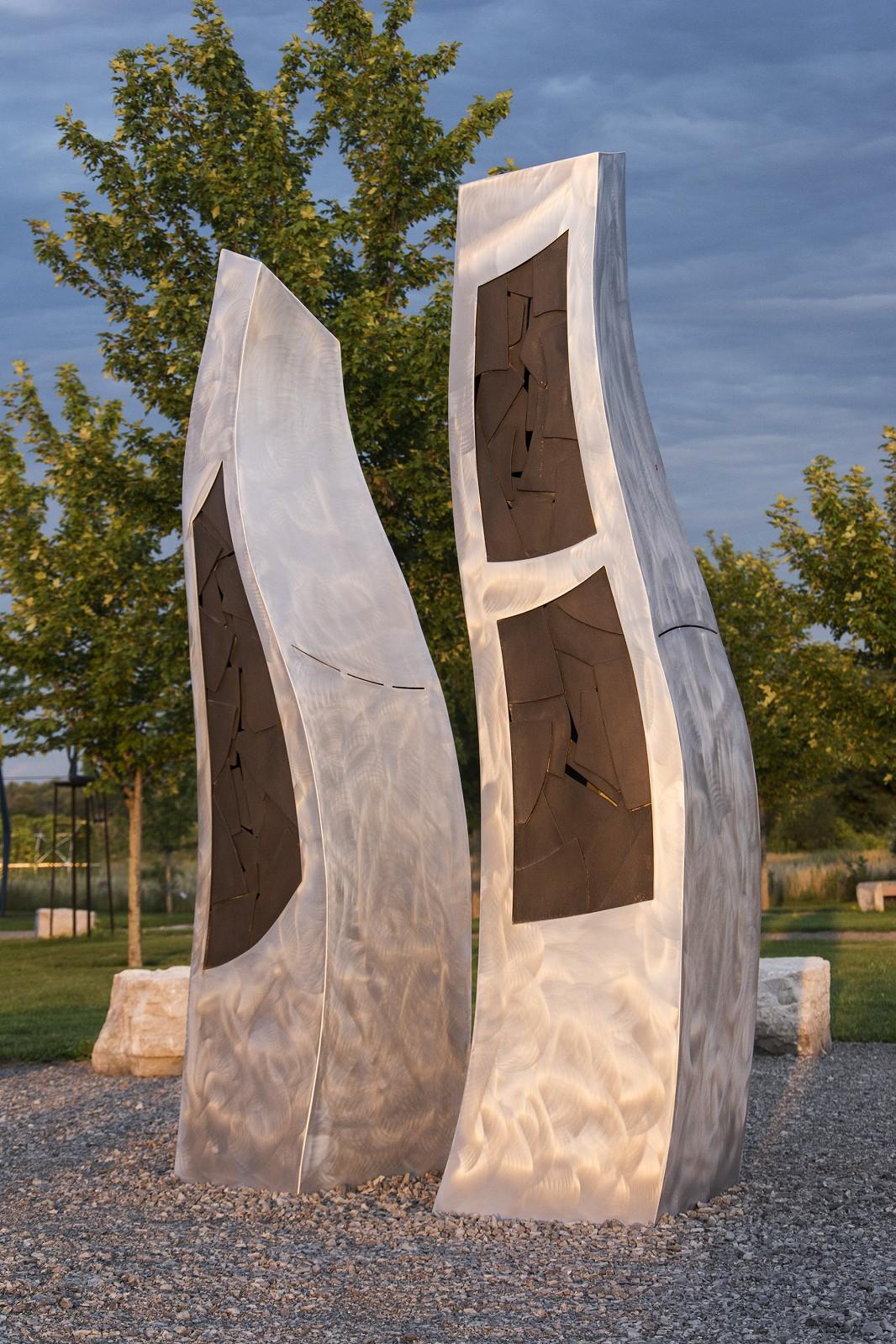 Deux formes organiques s'élèvent du sol et s'élèvent vers le ciel dans cette sculpture en aluminium finement travaillée de Stéphane Langlois.  Les formes abstraites évoquent l'idée de deux humains engagés dans une danse, peut-être deux oiseaux, se