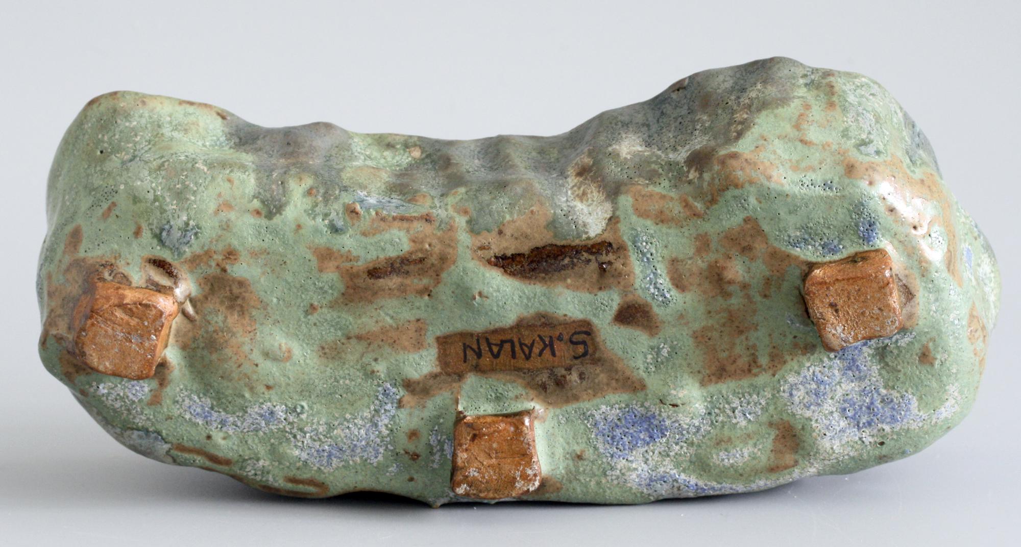 A stylish Brutalist sculptural form studio pottery open work bowl by Stephanie Kalan (1909-1978) probably dating 1953-1978. The bowl stands raised on three rough square cut feet and is formed in thick hand formed clay and decorated in green, blue