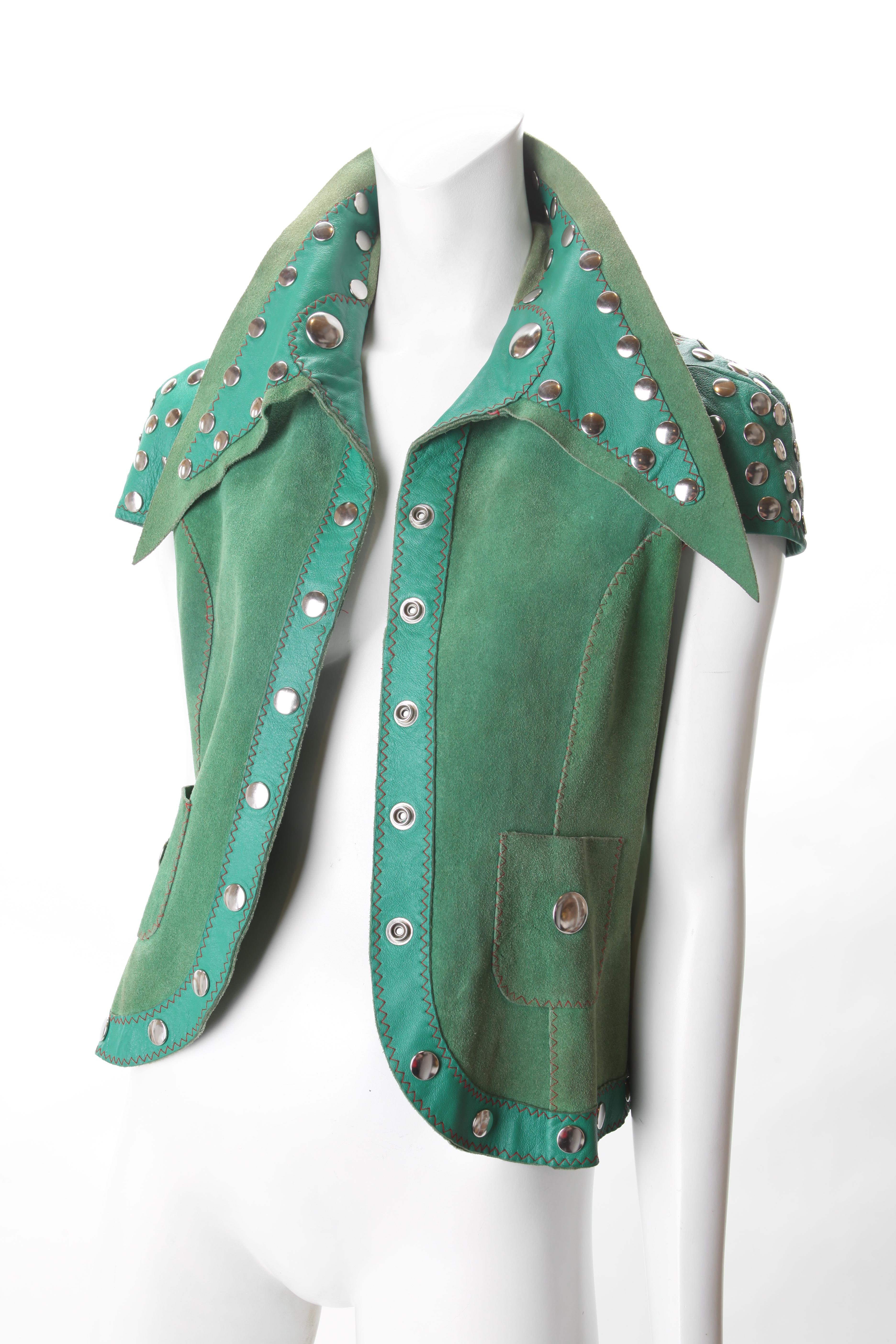 Stephen Burrows Green Suede & Leather Studded Vest, c.1970s.
Stephen Burrows Suede Vest features contrasting leather accent detail at sleeves, exaggerated collar and lapel/hemline. Vest has silver studded buttons with Silver studs adorning the
