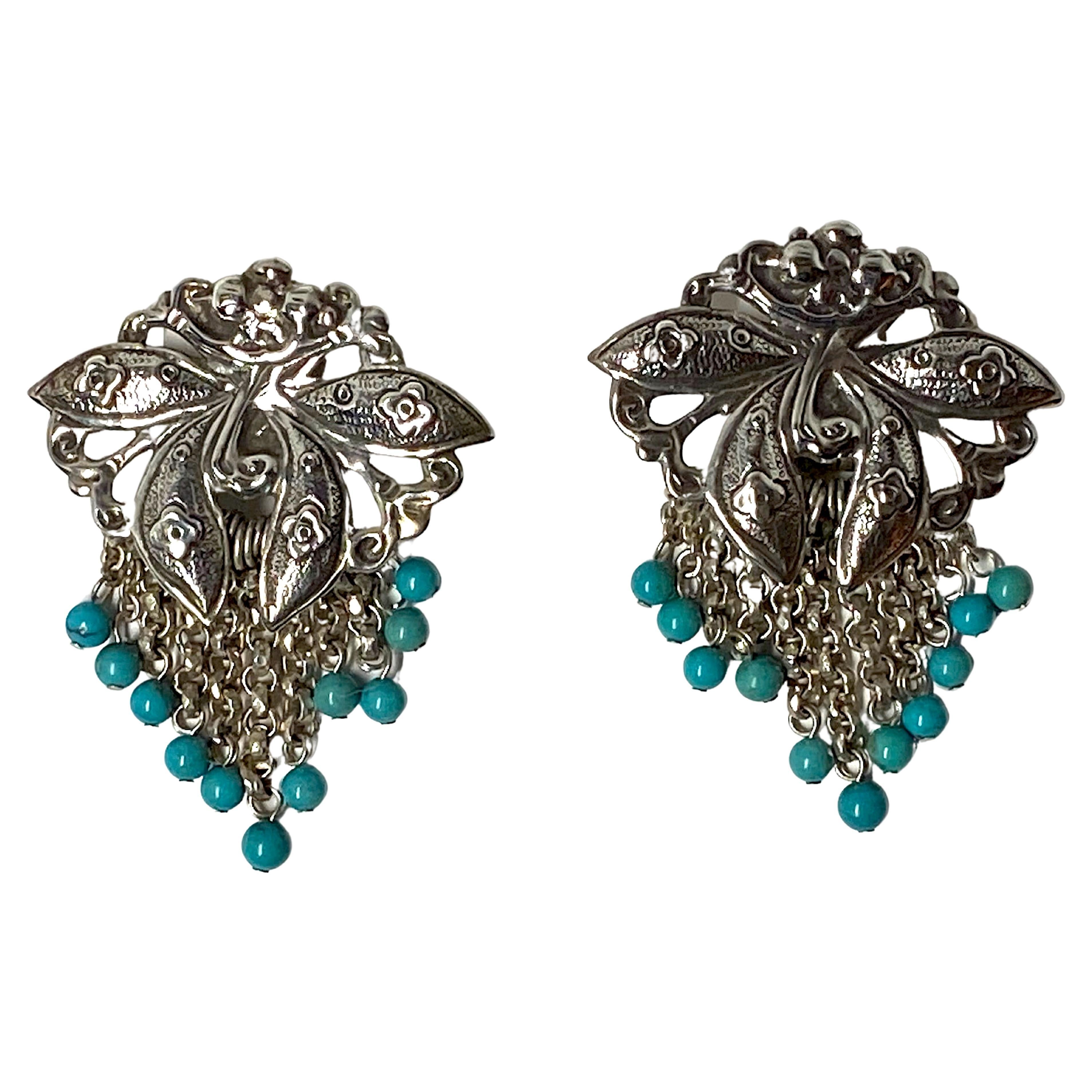 A lovely pair of sterling silver flower motif fringe earrings with turquoise beads from 1988 by famous American jewelry house Stephen Dweck. Each earring top is a stylized flower with four petals and has fringe chain descending from it finishing