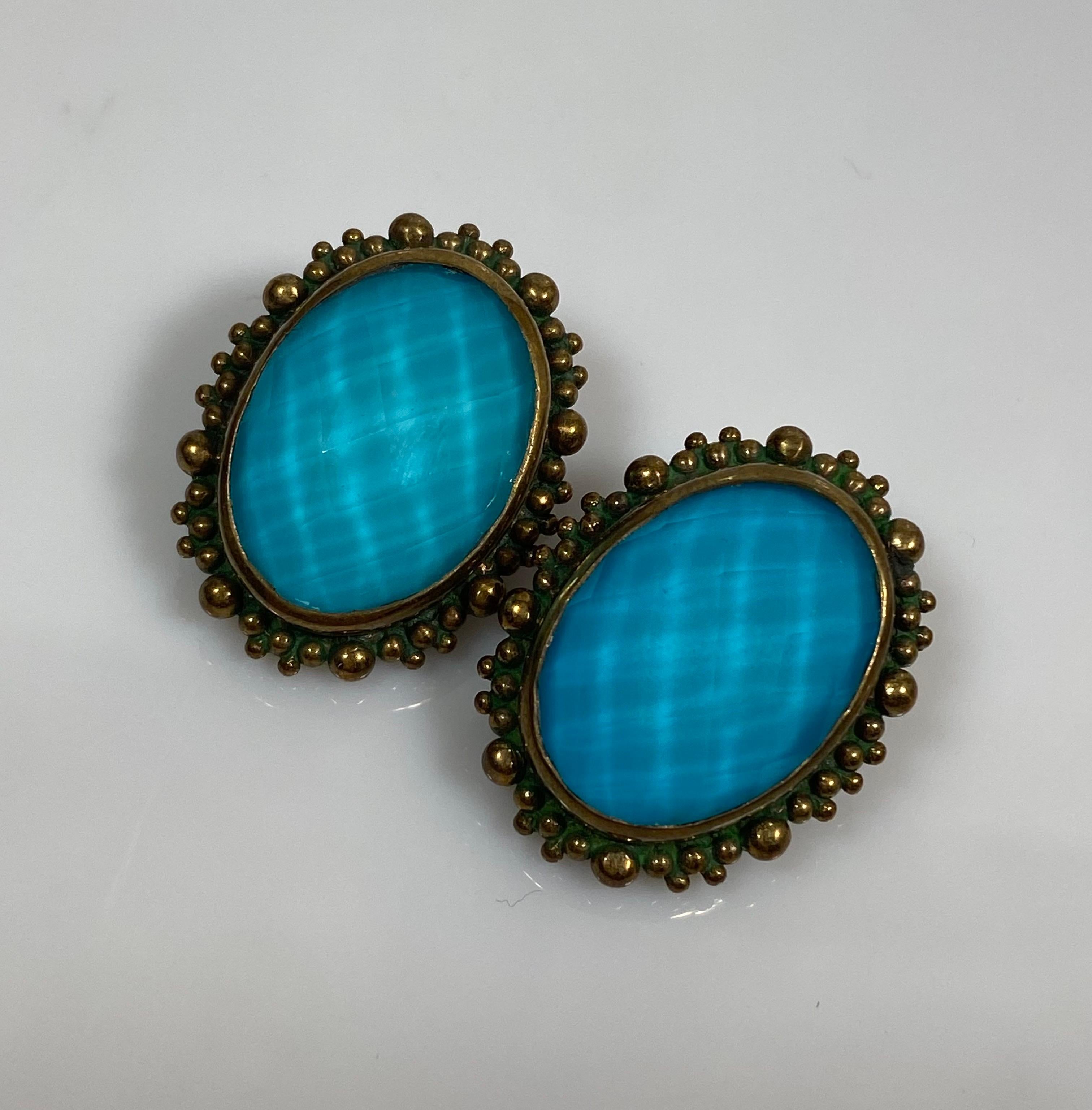 These 2001 Stephen Dweck earrings are sterling silver with a bronze overlay and a faceted turquoise textured oval shape. Around the main faceted stone is a bronze textured trim and there is a textured back and bronze clip. These vintage earrings are