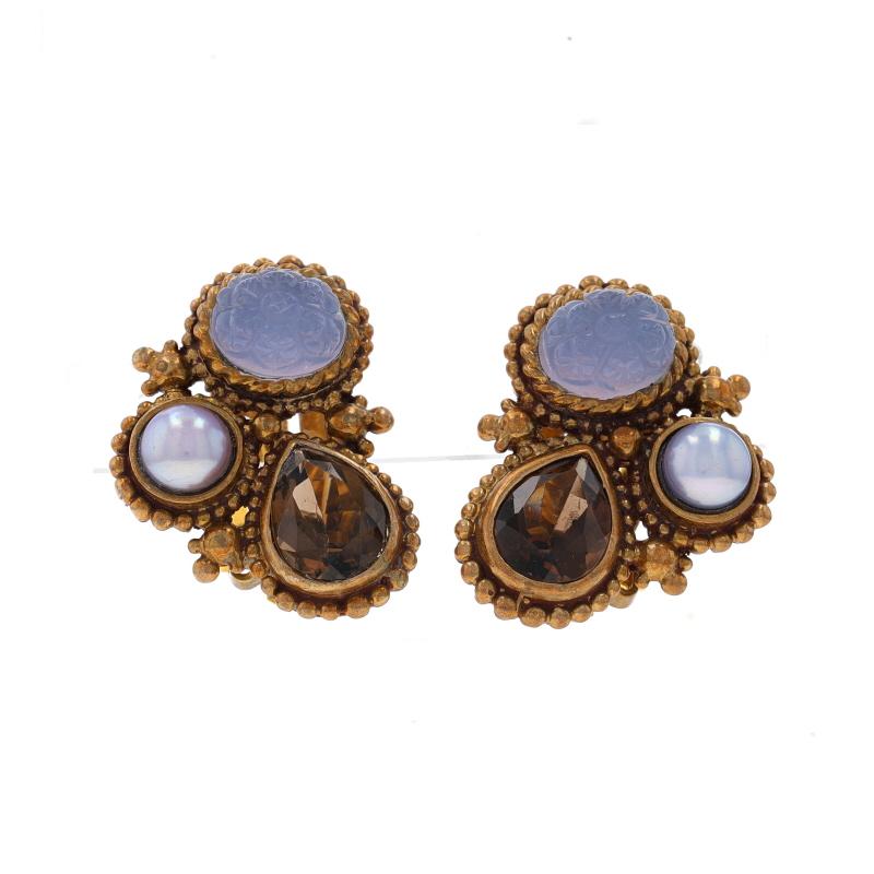 Brand: Stephen Dweck

Metal Content: Brass & Sterling Silver (gold plated)

Stone Information
Natural Chalcedony
Cut: Carved Cabochon
Color: Purple

Cultured Freshwater Pearls
Color: Greyish Purple

Natural Smoky Quartz
Cut: Pear
Color: