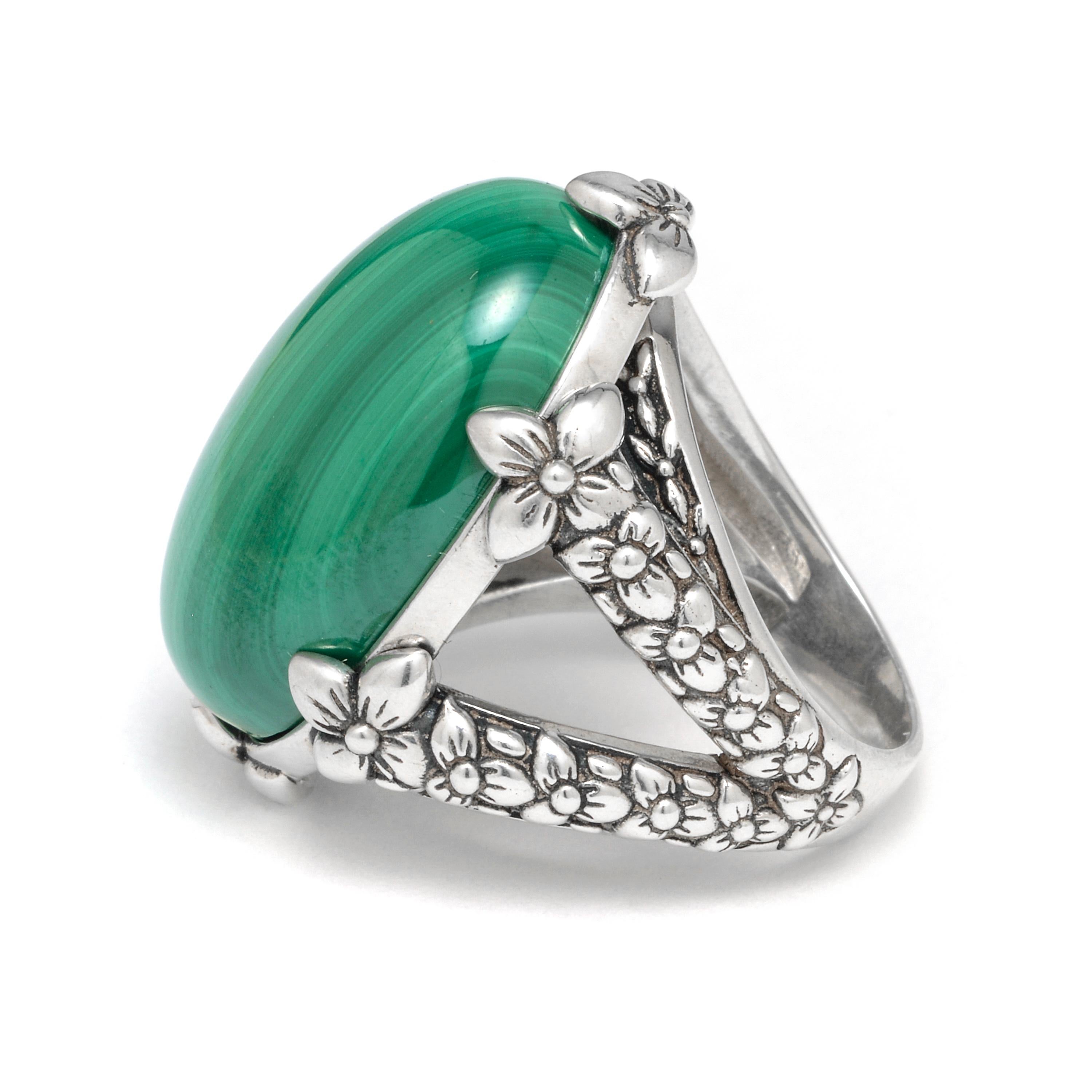 This bold Stephen Dweck Sterling Silver Statement Ring features a vibrant Malachite cabochon (18mm x 26mm) held by double shanks of sterling silver adorned with floral detail. Drawing inspiration from a love of nature and passion for art, each