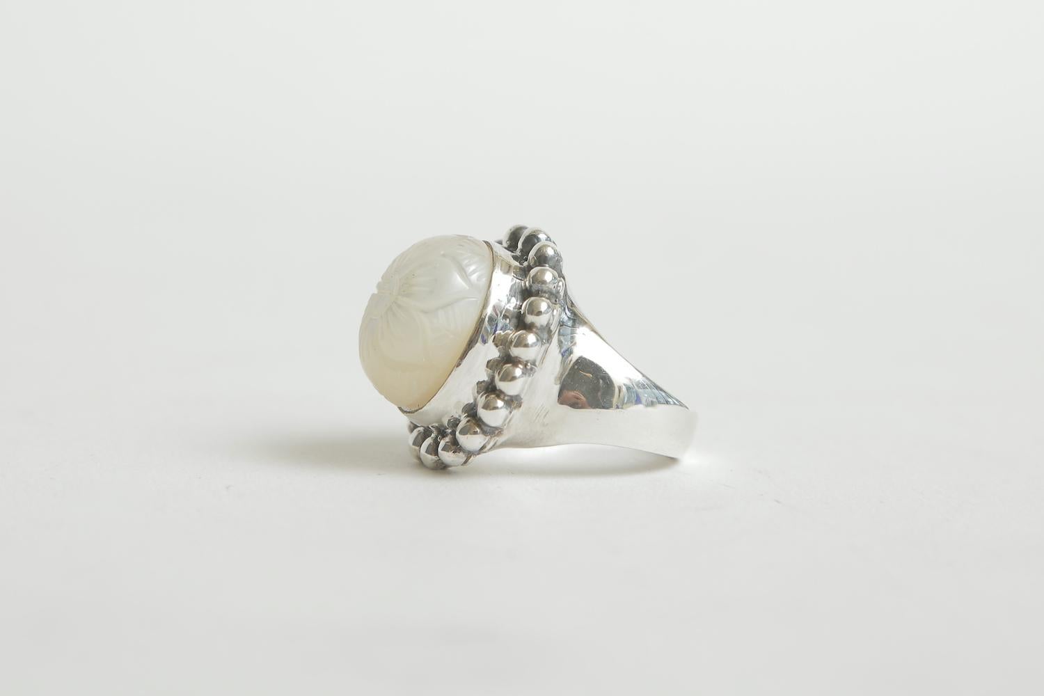 This very beautiful and substantial dome ring by the NYC based jewelry designer Stephen Dweck is a combination of sterling silver and intaglio mother of pearl in a flower design. It sits large on your finger in height and presence. It can be resized