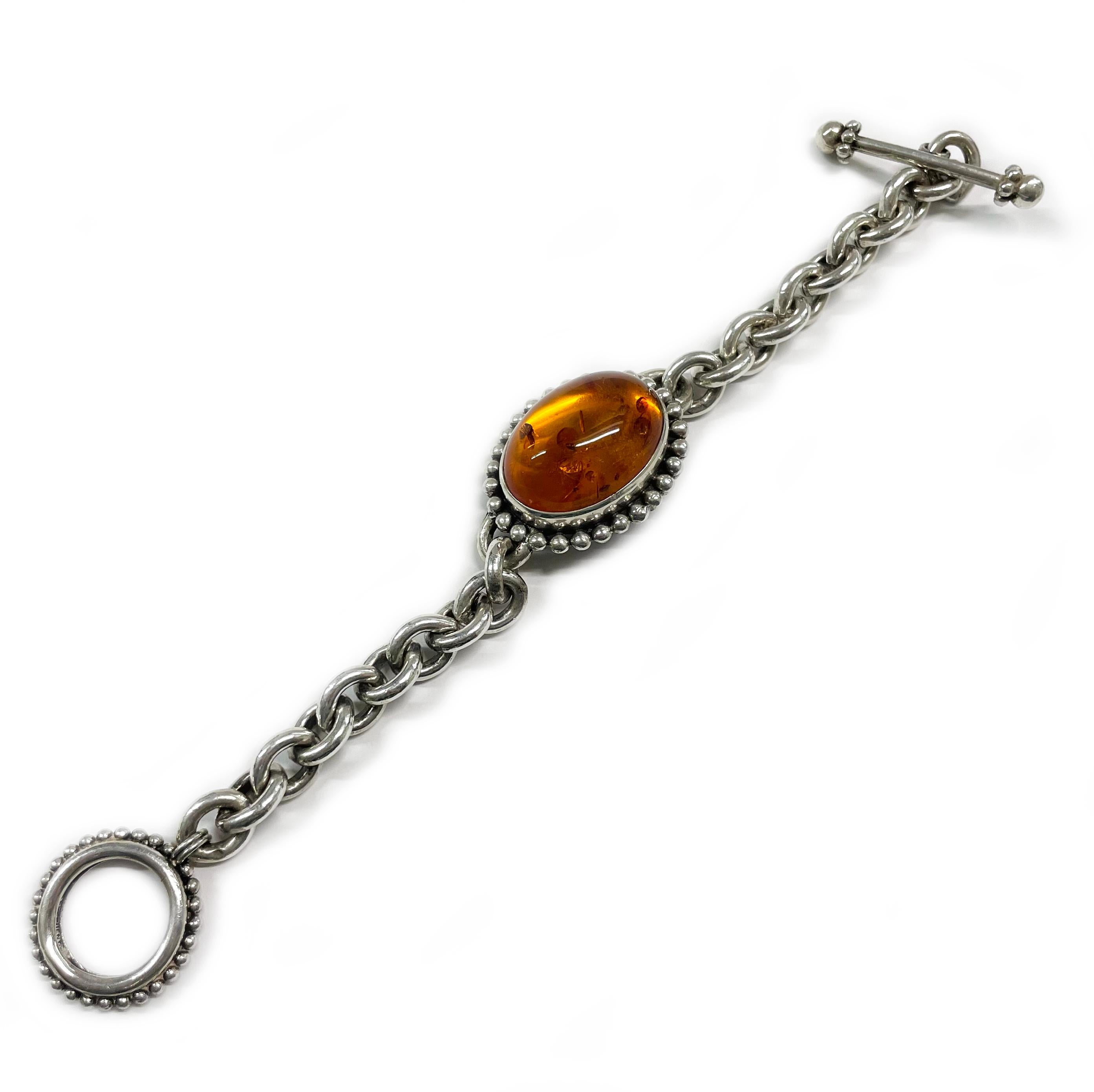 Stephen Dweck Sterling Silver Baltic Amber Bracelet. The large oval Baltic Amber cabochon is bezel-set with a beaded surround. The Amber cabochon measures approximately 25 x 19mm. The bracelet features a chain-link with an oval bezel connector with