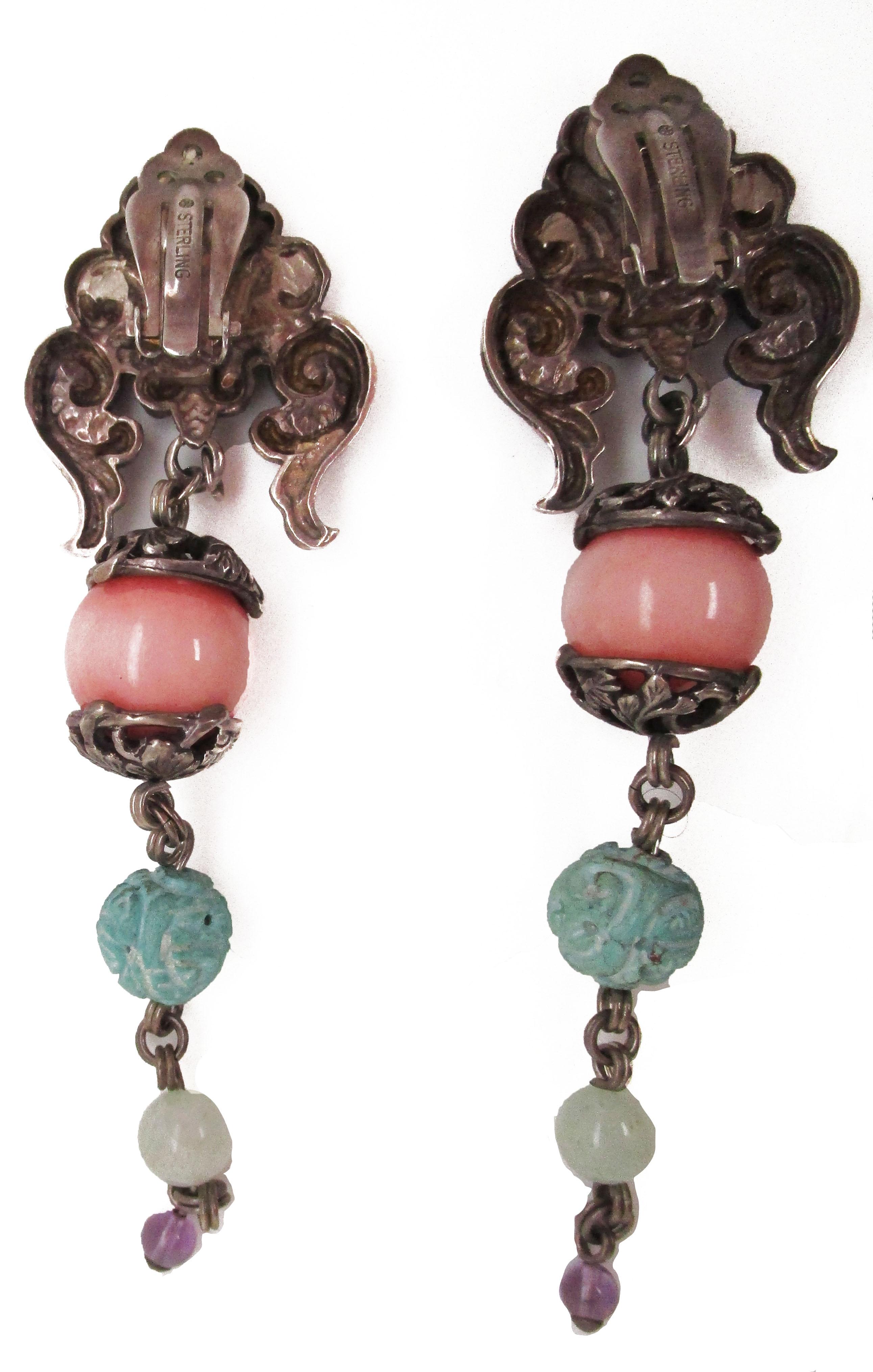 These gorgeous vintage Stephen Dweck runway earrings feature a brilliant combination of sterling silver, carved turquoise, jade, and amethyst in a dramatic dangle style. These clip-on earrings have a dramatic, long large to small graduated center