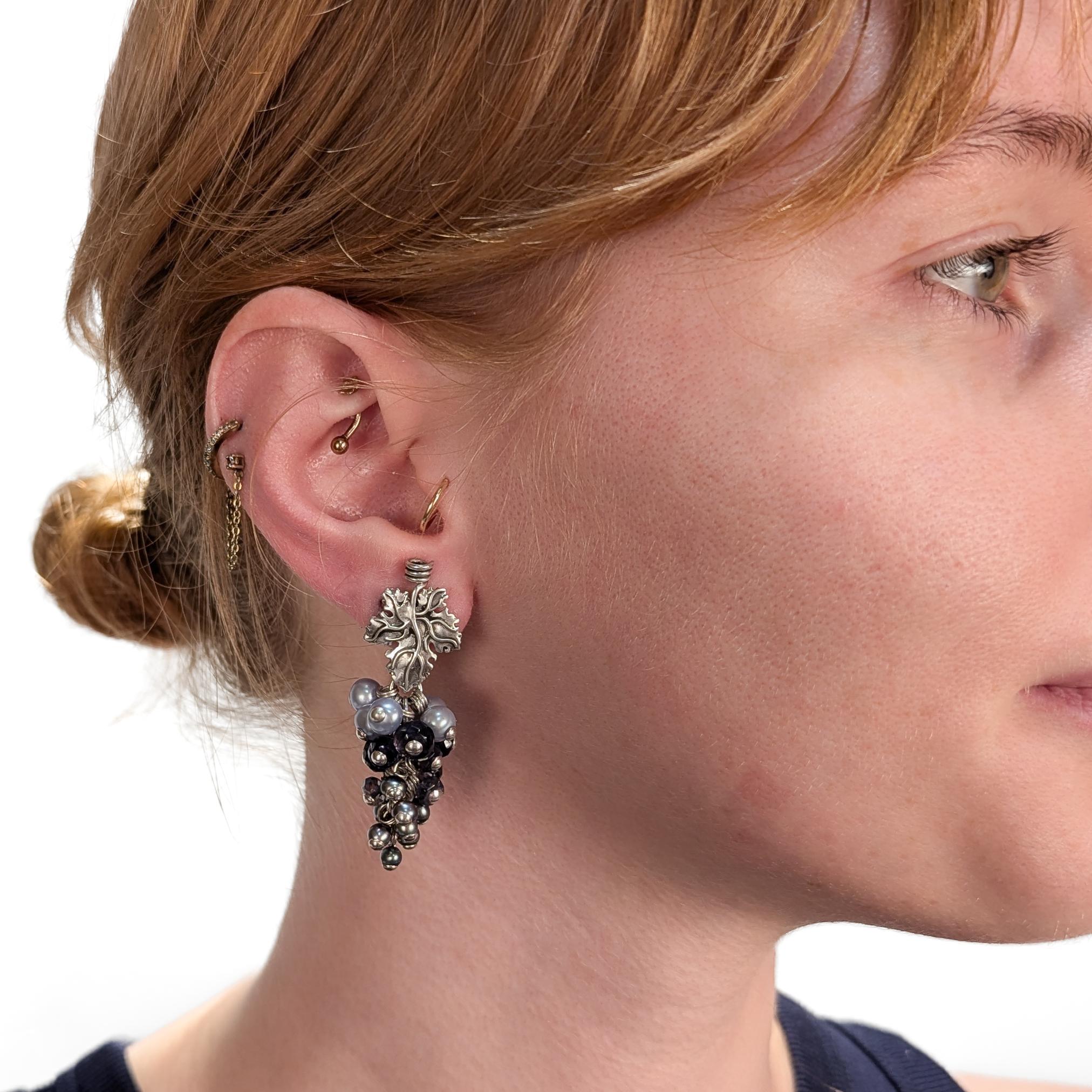 A fine pair of signed silver, gemstone, and tahitian pearl earrings.

By Stephen Dweck. 

In sterling silver.

In the form of grapes or berries with tahitian pearls in gray and light blue, and a purple-blue gemstone. The clips at the top with