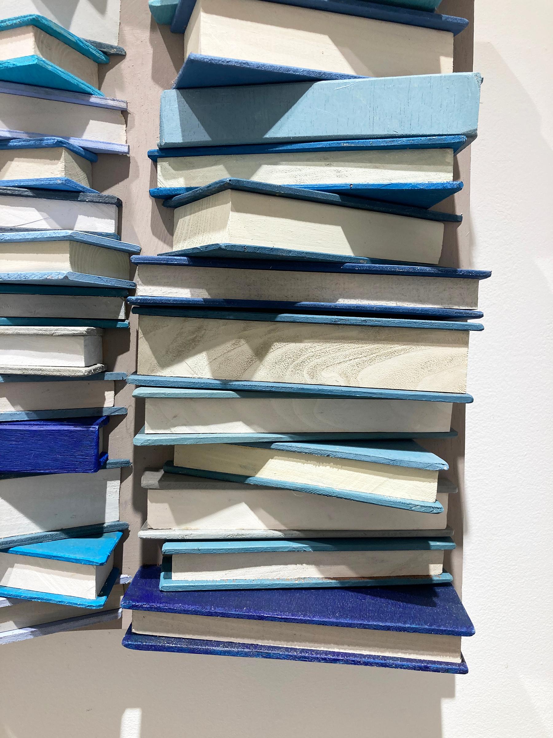 Abstract geometric three-dimensional wood wall sculpture resembling stacked books in blue, grey, and white 

