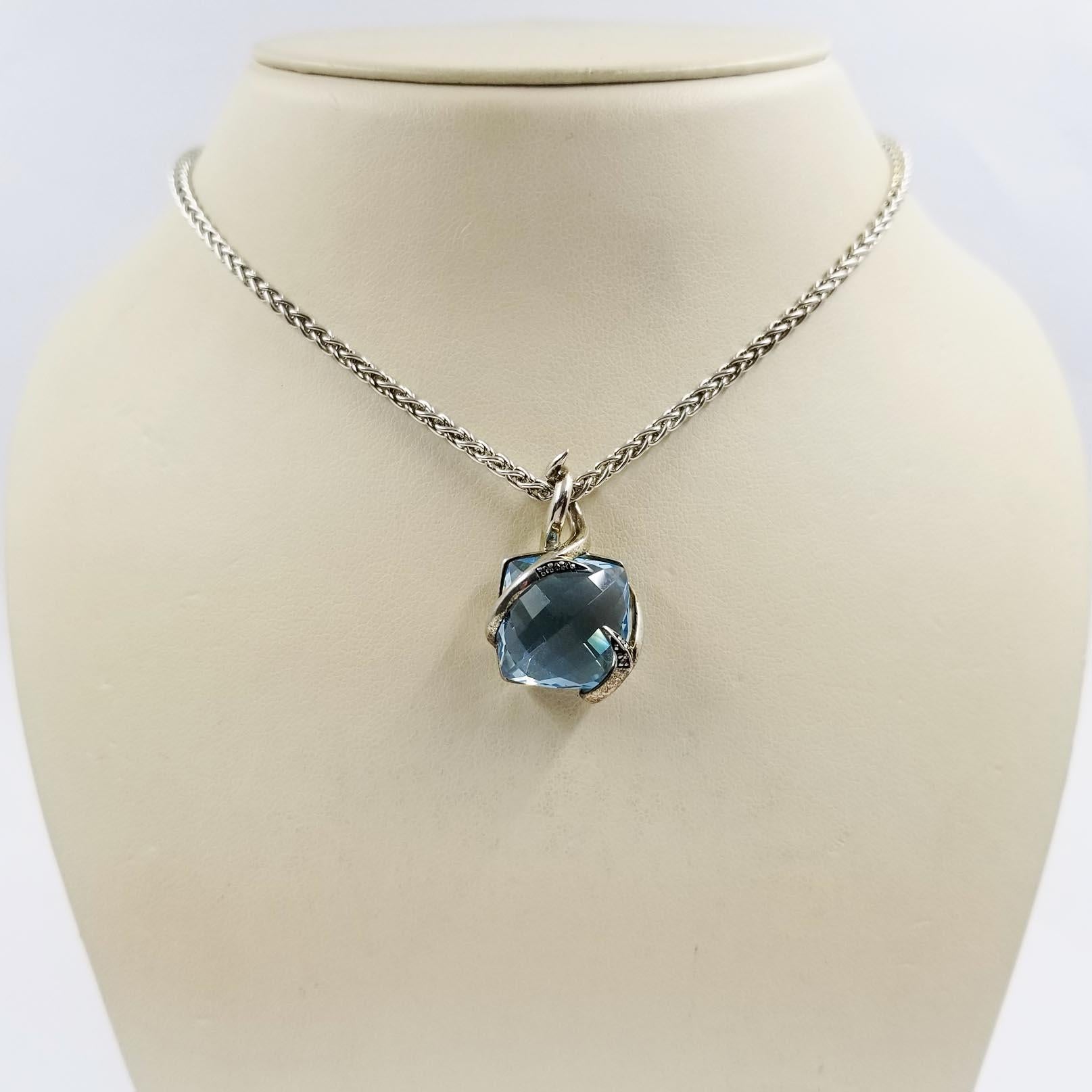 This simple pendant necklace is crafted in sterling silver by designer Stephen Webster. It features a 0.5 inch by 0.5 inch checkerboard cushion cut blue topaz center stone. The topaz is held in place by two wrapped diamond encrusted thorns. The