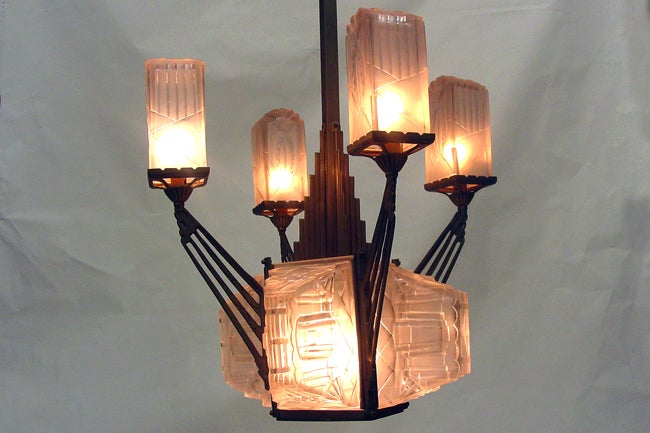 This early Art Deco chandelier features a stepped nickel body with four radiating arms each finished with an intricate frosted glass shade. The fixture has eight glass panes in total each are signed “Hugue” Along with each arm, the center of the