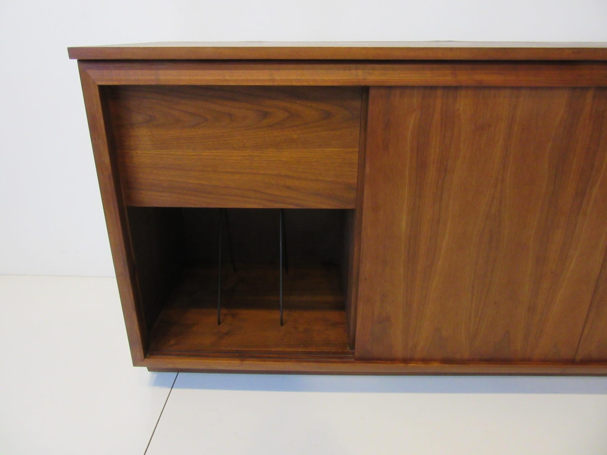 A well designed midcentury walnut stereo / record cabinet with three sliding doors each side has a built in record rack. The center section has shelves for your components and the the top flips open reveling storage or more space for other