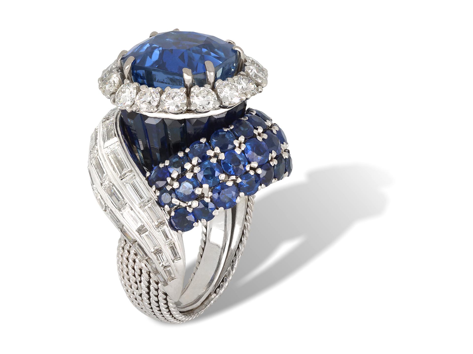 Anello Sterlé con zaffiro e diamante. Al centro è incastonato uno zaffiro Ceylon naturale non valorizzato a forma di cuscino in un'incastonatura a doppia griffe aperta sul retro con un peso di 8,67 carati, circondato da sedici diamanti rotondi