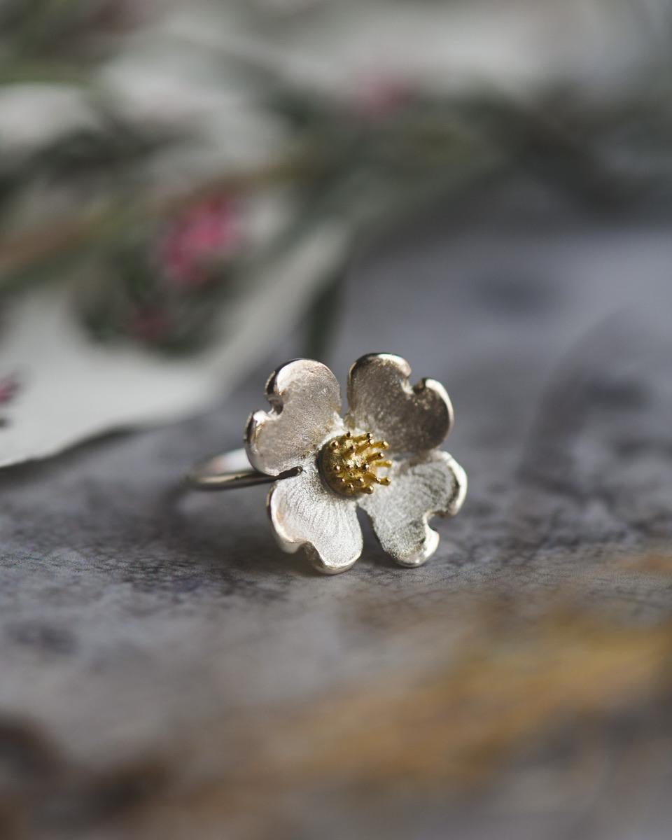 Nestled in your palm lies more than jewelry. It's a moment captured in precious metal. This dogwood promise ring features sterling silver petals, each one meticulously crafted to reflect the legendary dogwoods four petal bloom. At the center, a warm