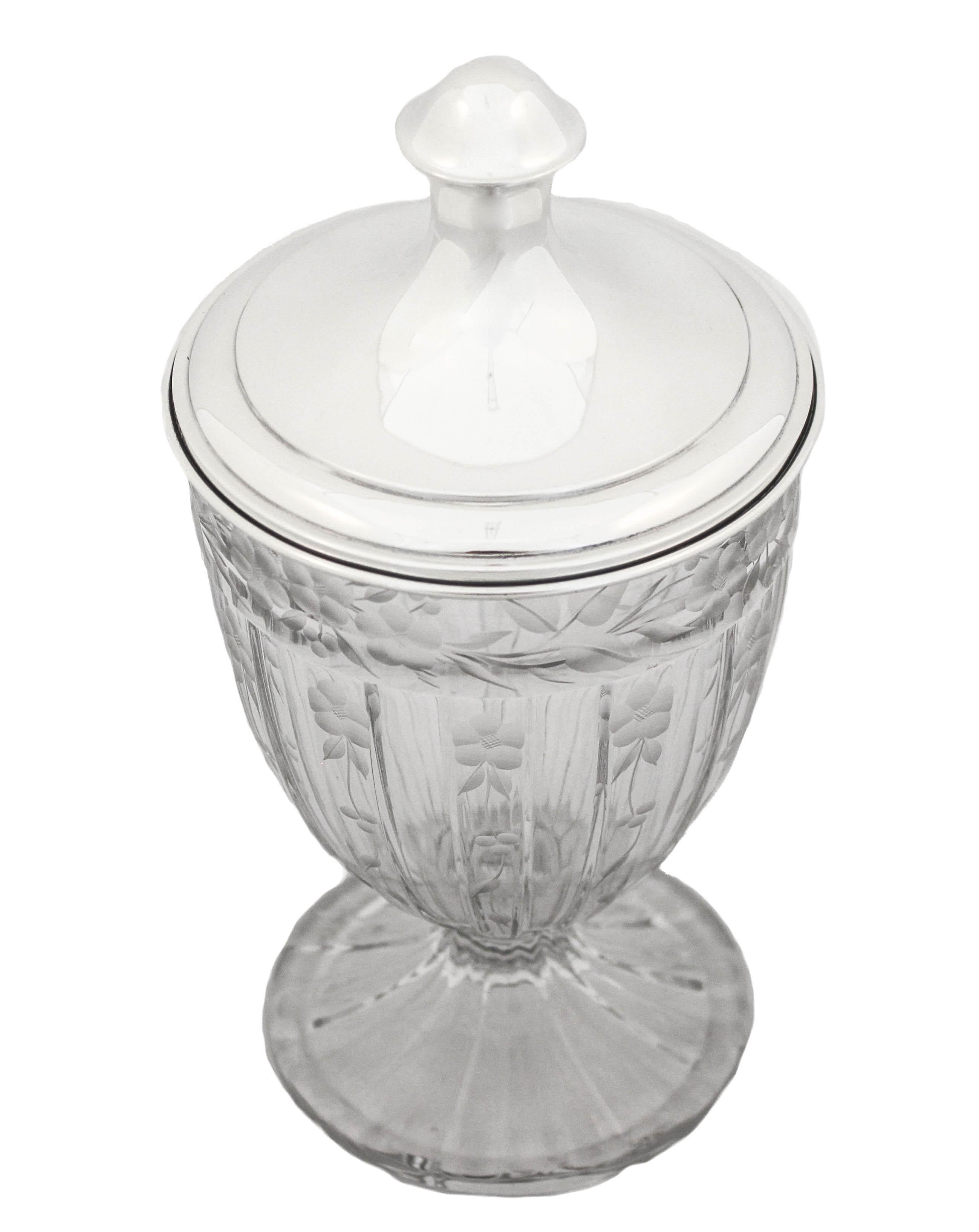 This beautiful crystal urn with a sterling silver lid manufactured by the Hawkes Glass Company. 
Based in Corning, NY, T.G. Hawkes & Co. (c.1880-1959) was established by Thomas Gibbons Hawkes (1846-1913). Born in Ireland, Hawkes immigrated to