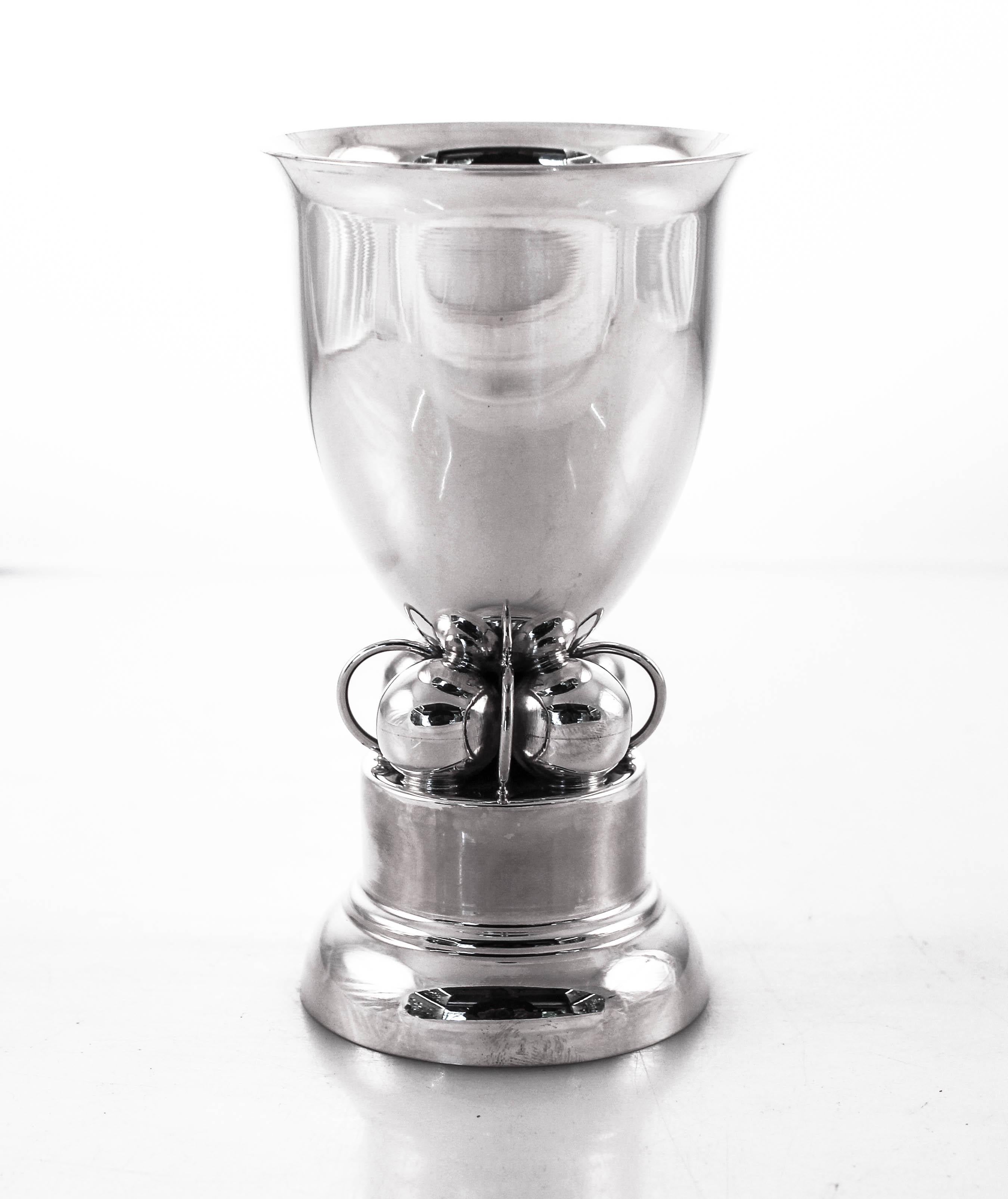 This lovely sterling silver goblet has a Art Deco design. It has four balls in the center intercepted by rings. It stands on a non-weighted base that gives it a tall regal appearance. If I were to describe it in one word, “Jensenesque”. The inside