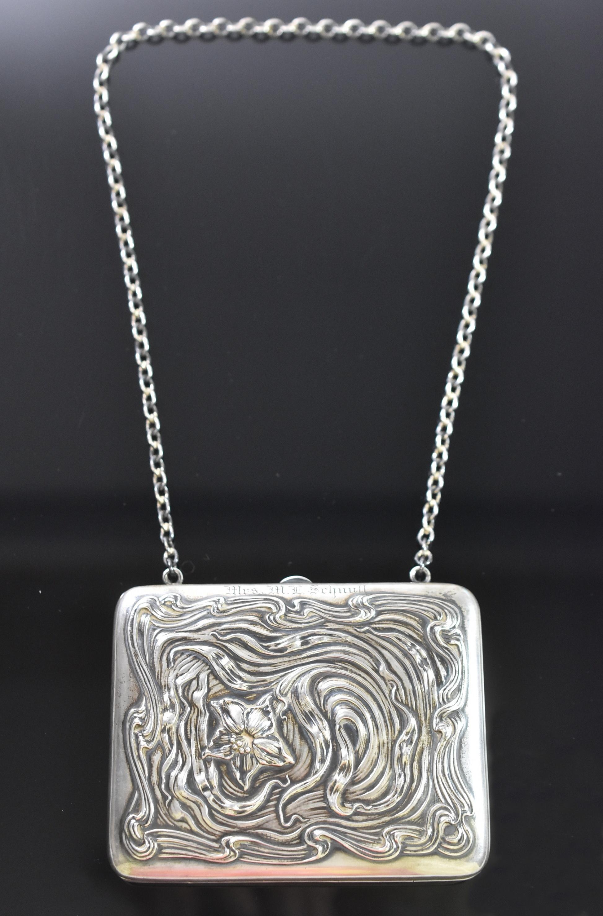 Questo bellissimo borsellino in argento sterling con catena può essere utilizzato anche come portasigarette. La borsetta è decorata con un fiore e un nastro ondulato ed è in ottime condizioni. C'è un leggero monogramma sul bordo, vicino alla