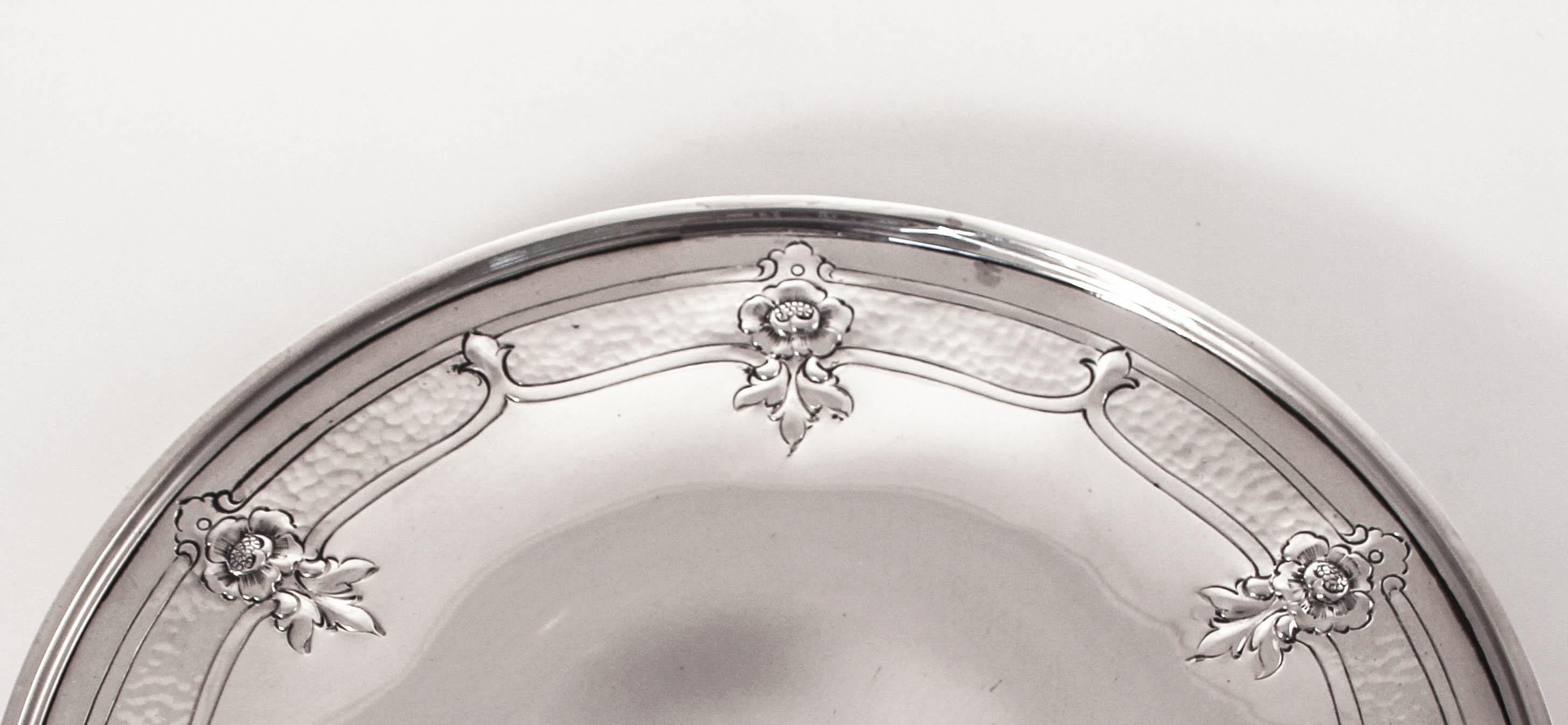 A lovely antique piece designed by Wallace Silversmiths of Wallingford Connecticut. It has a hammered design going around the edge with six flowers and Fluer De Lis rotating in-between. The tray stands on a center pedestal raising it off the