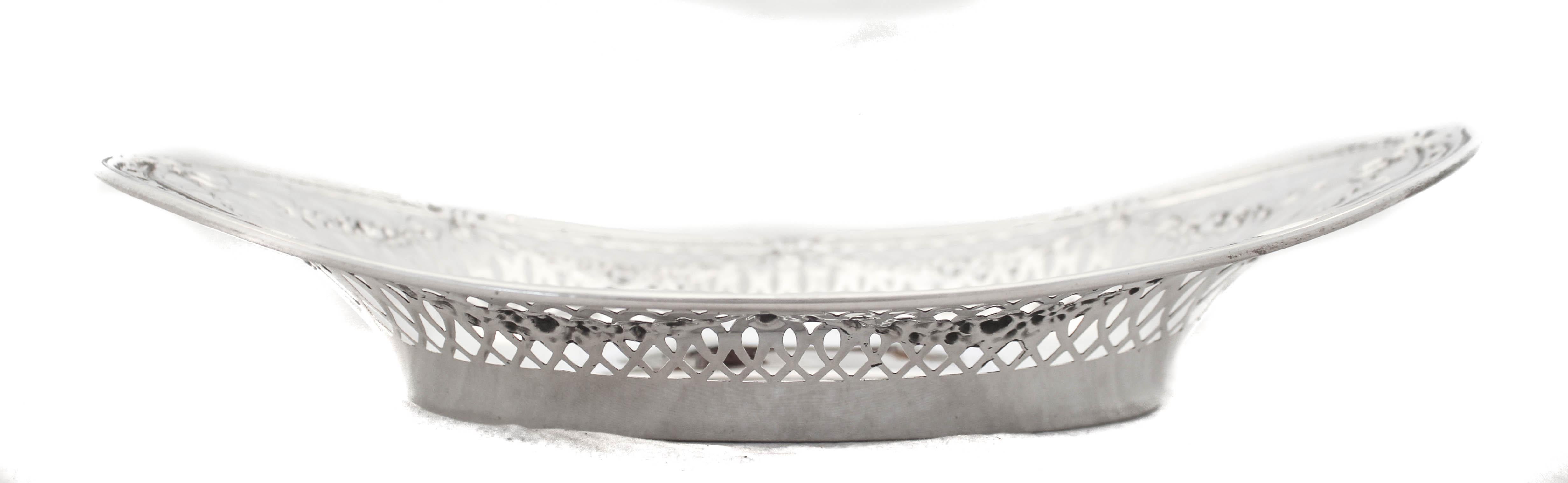 A beautiful sterling silver breadbasket by the Webster Silver Company; it is ornate and elegant. It has a geometric cutout pattern around the body with garlands draping over. Along the outer rim a motif of interlocking circles goes around the