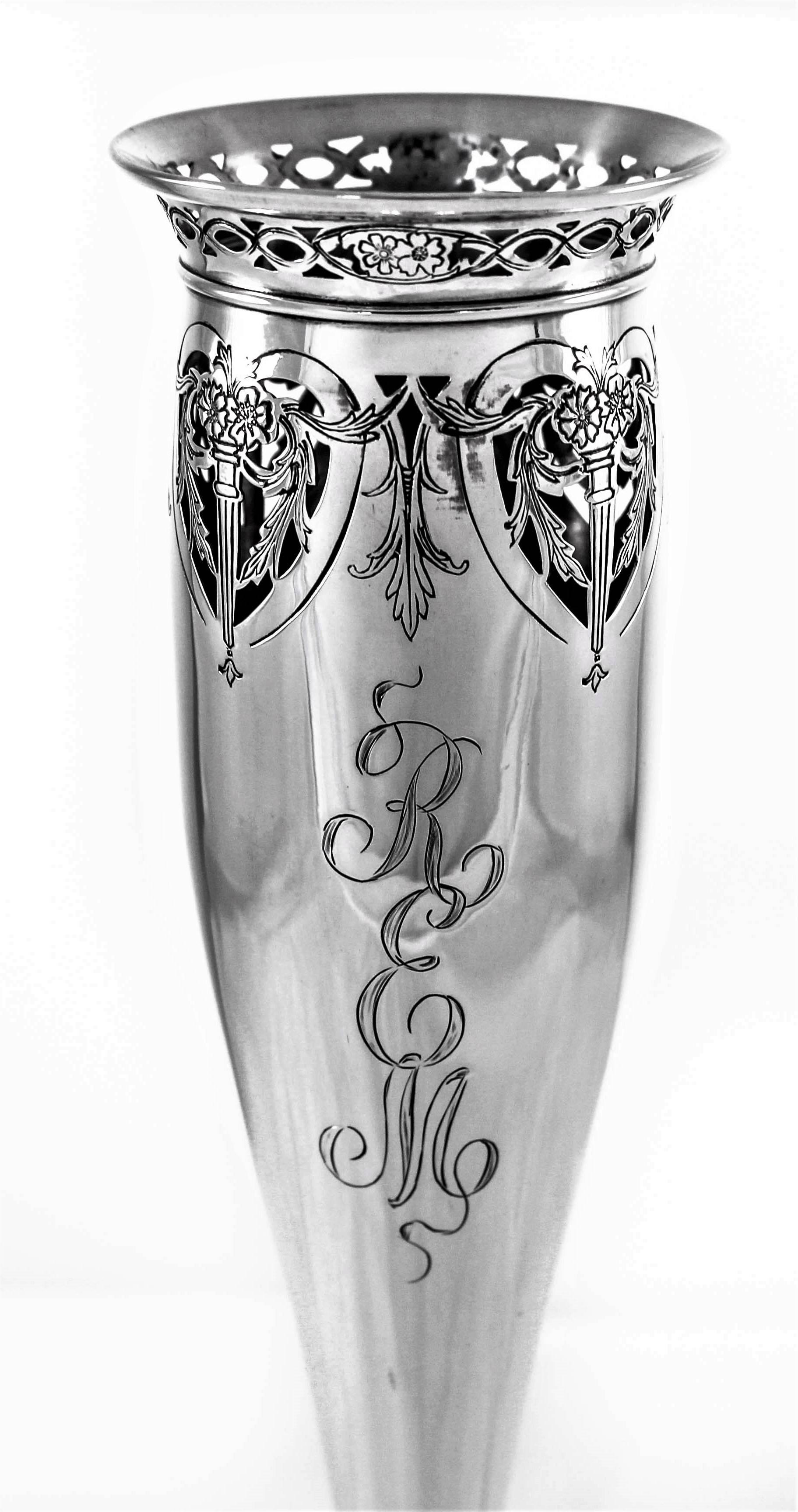 This bud vase has a very feminine silhouette with a tapered bottom. Around the top there is a ring of lattice work around the edge and beneath that heart-shaped cutouts with flowers and leaves. In the center a hand engraved monogram in a lovely