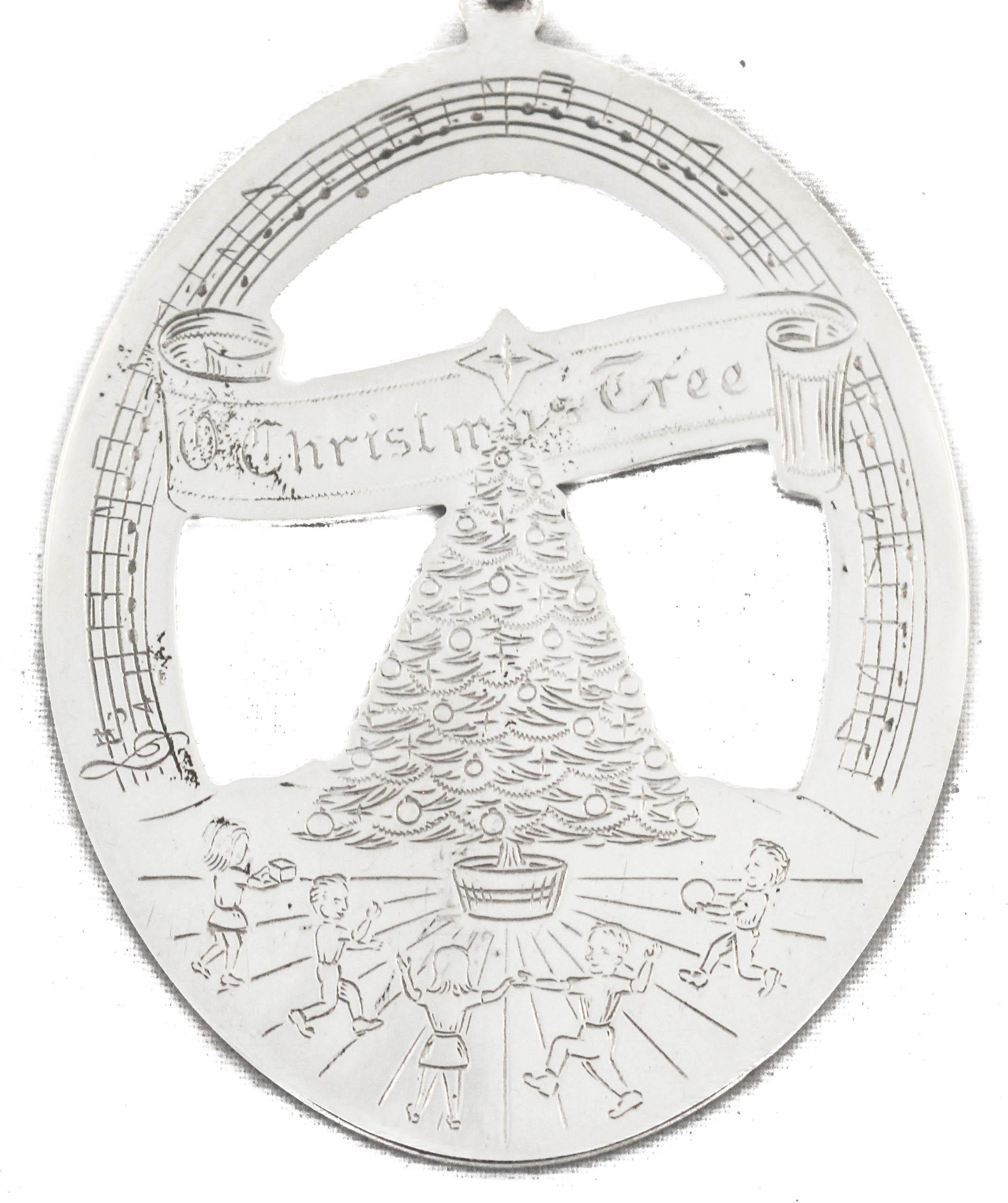 Nous sommes heureux de vous offrir cette décoration de Noël en argent sterling de 1978 par Lunt Silversmiths. La forme est ovale avec une découpe au milieu. D'un côté, le long du bord supérieur, on peut lire 