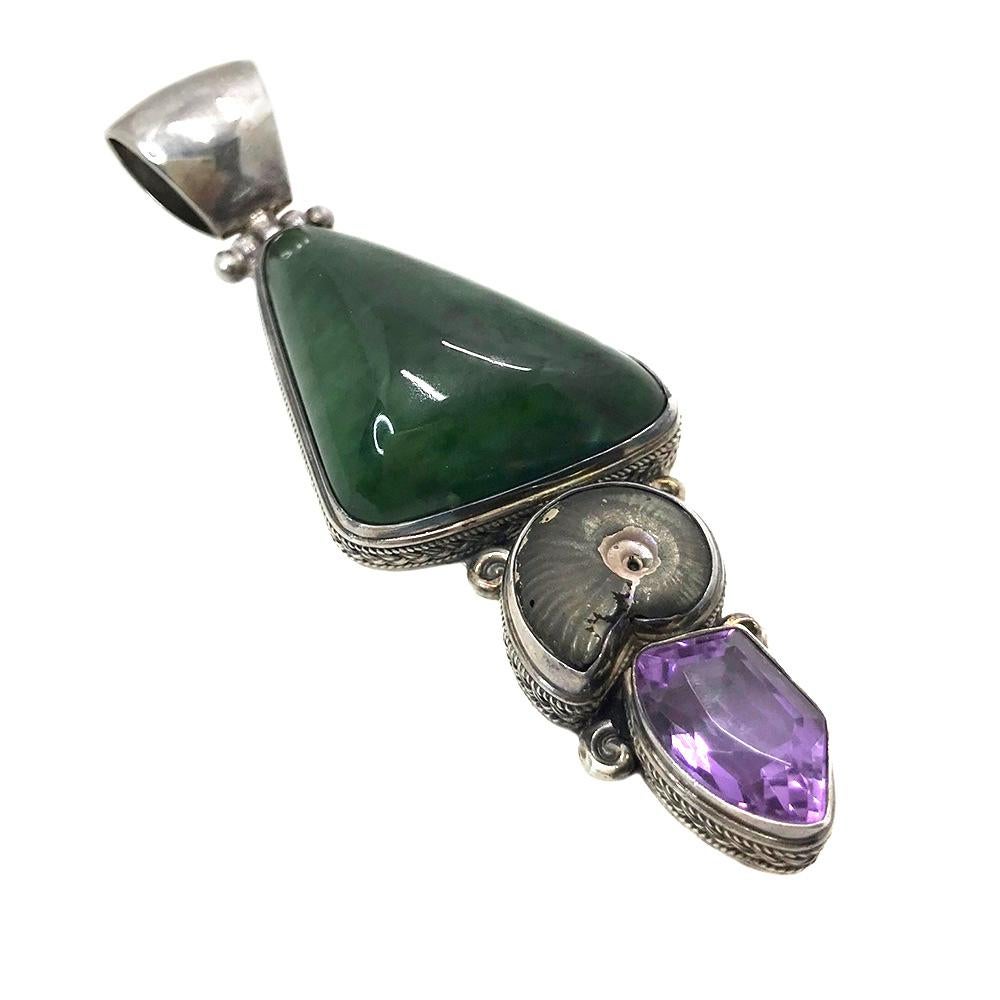 This is a sterling collar necklace with jade and amethyst pendant. The sterling pendant has a large triangle tumbled jade, a smaller ammonoidea and an irregular shaped shield cut transparent faceted amethyst set in a finely detailed sterling frame.