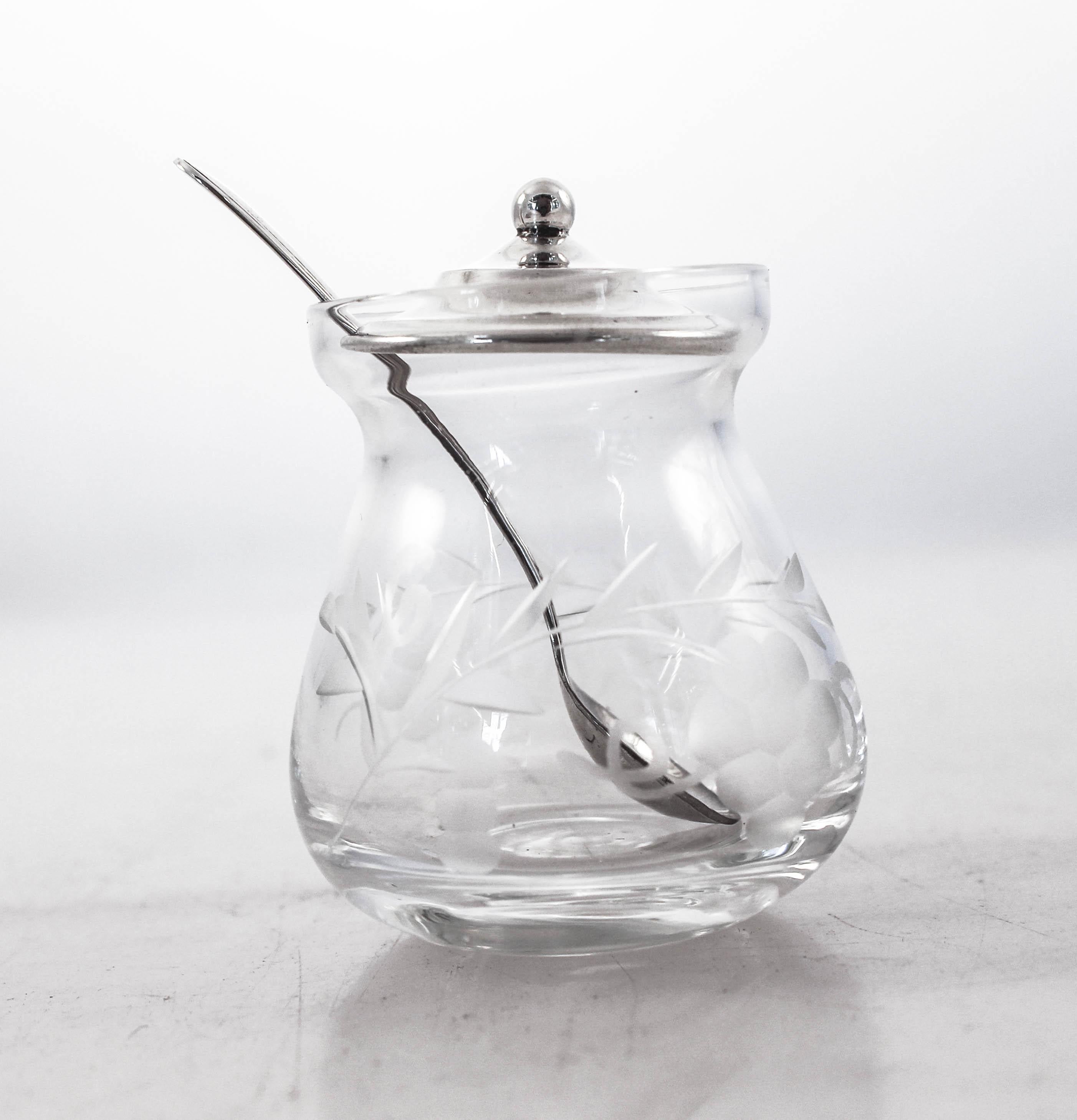 A beautiful and delicate crystal mustard jar with a sterling silver lid and spoon. The crystal has an acid-etched design of leaves and vines. The sterling silver lid and spoon are simple and have no decoration. A nice juxtaposition from the old