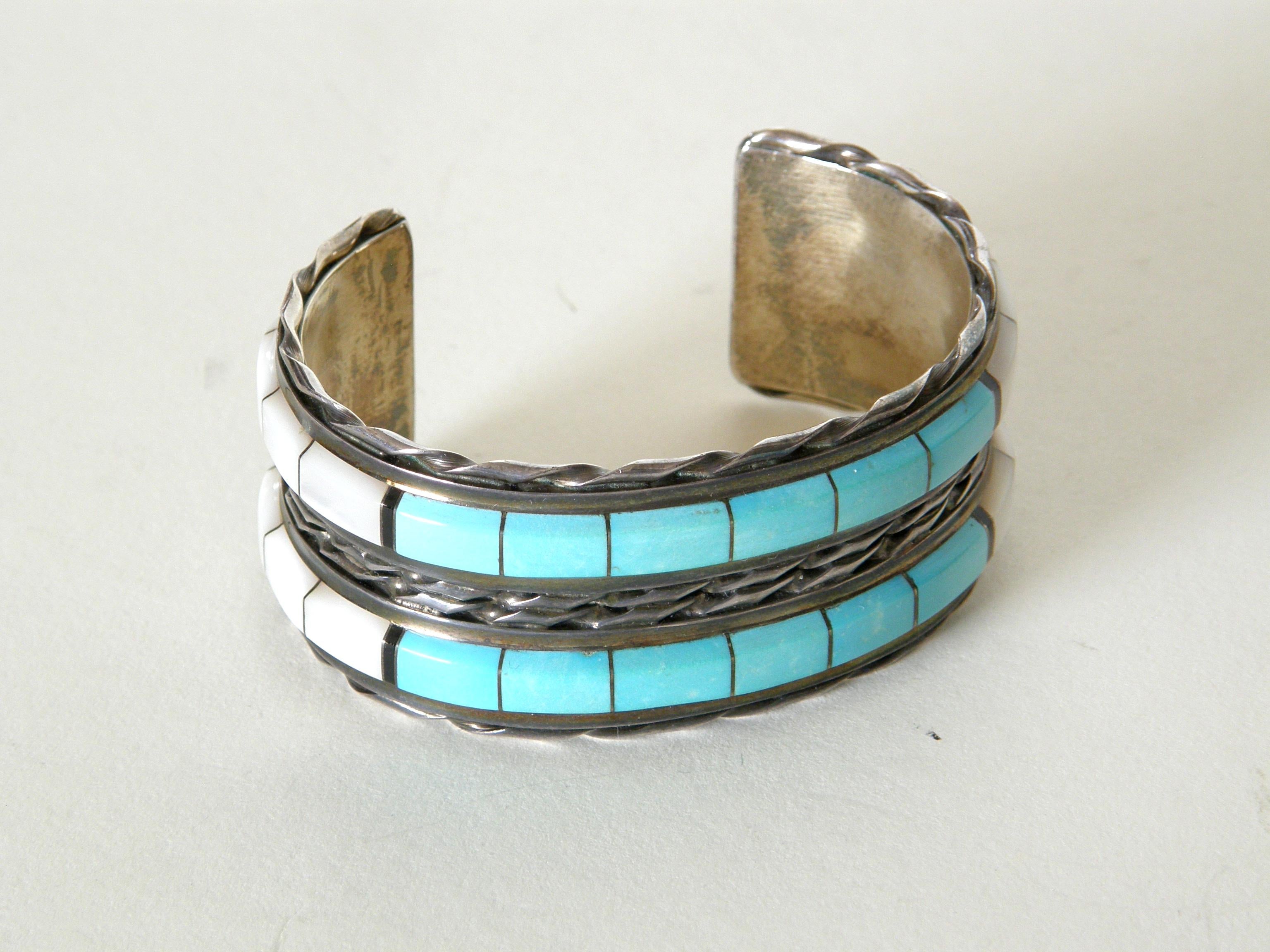 This handsome sterling silver cuff bracelet was made by Zuni artists Martin and Esther Panteah. The banded design features rows of turquoise and mother of pearl in a raised inlay. They are framed by rows of twisted bands of silver.

marked : “M T