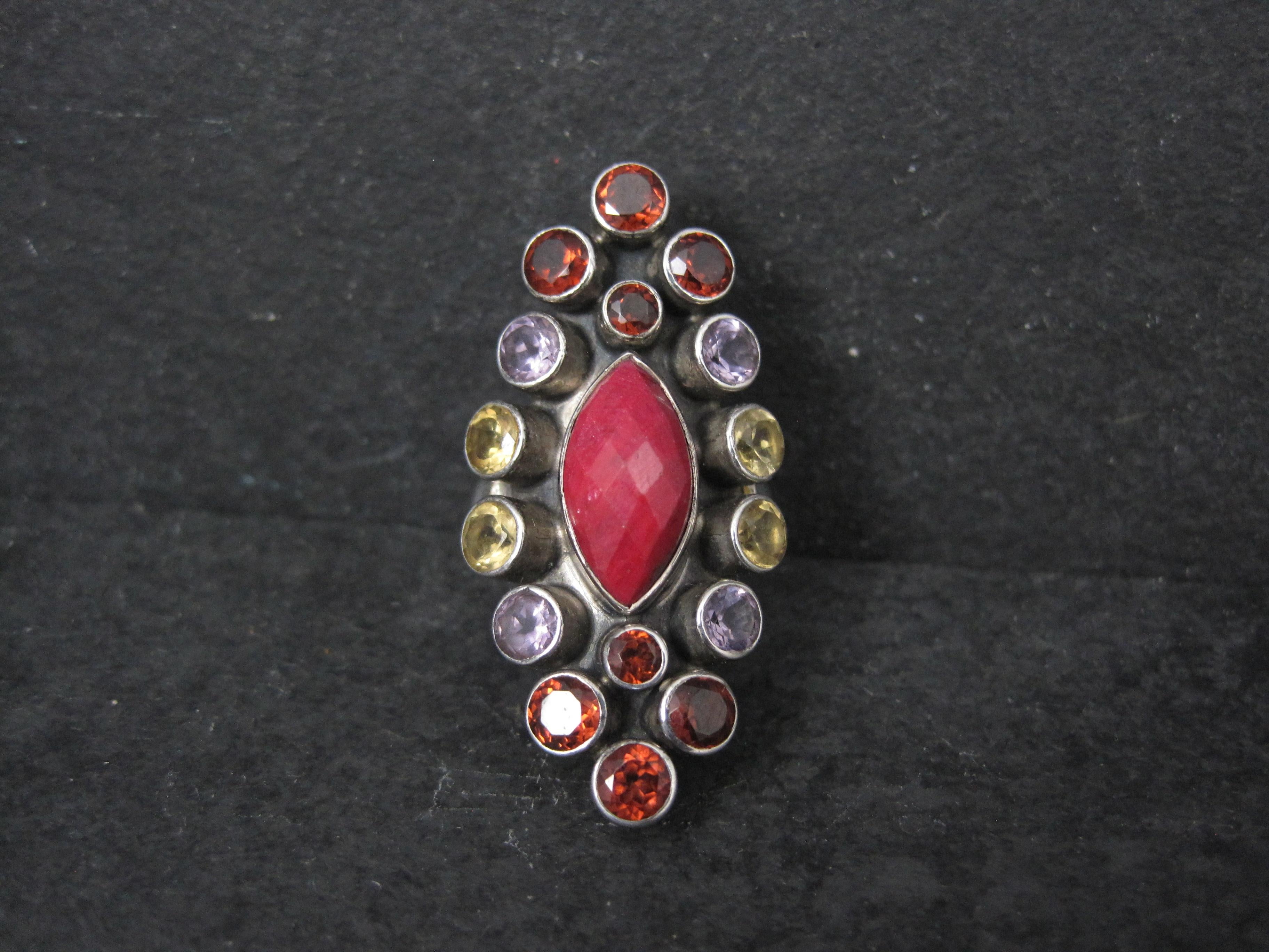Este precioso anillo es un producto de Nicky Butler.
Presenta un rubí facetado de 7x13 mm acentuado por granates, citrinos y amatistas.

La cara de este anillo mide 2,5 cm de norte a sur.
Talla: 6

Marcas: NB, 925, India

Estado: Excelente