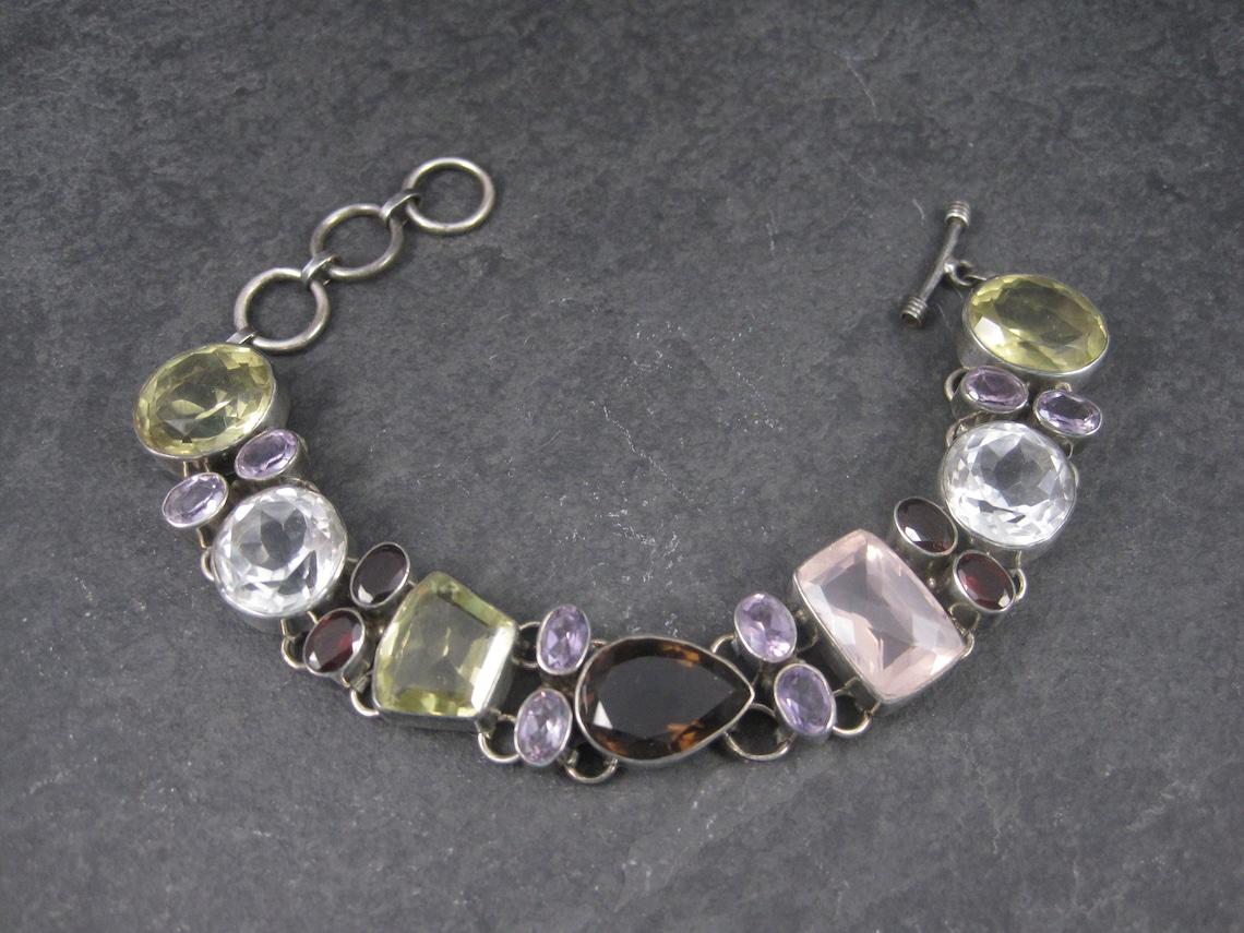 This gorgeous 90s gemstone bracelet is sterling silver.
It features citrine, amethyst, clear quartz, garnet, smoky quartz and rose quartz gemstones.

These gemstones are estimated to be apx 50 carats total.

Measurements: 11/16 of an inch wide
The
