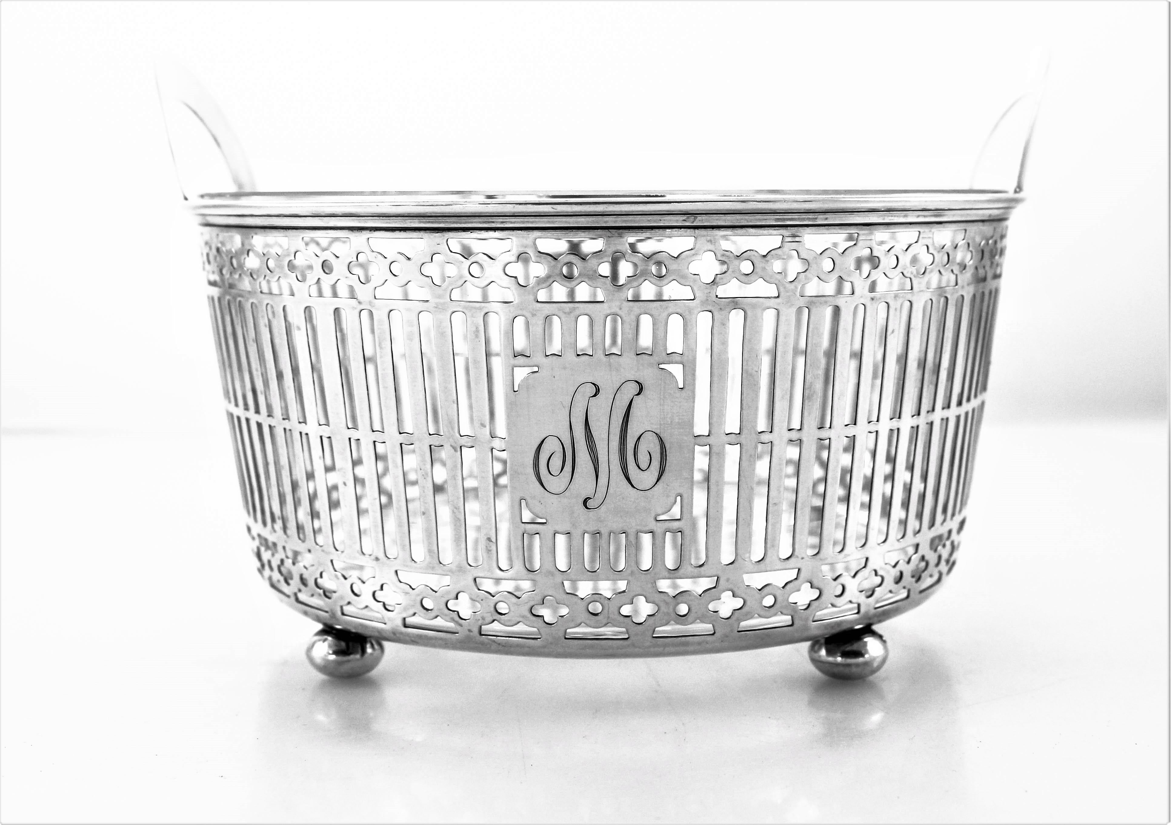 This sterling silver ice bucket has a lattice pattern going around the entire circumference. On each end there is a semi-circular handle to hold and pass it around. It stands on four ball-feet that props it off the surface. The crystal liner comes