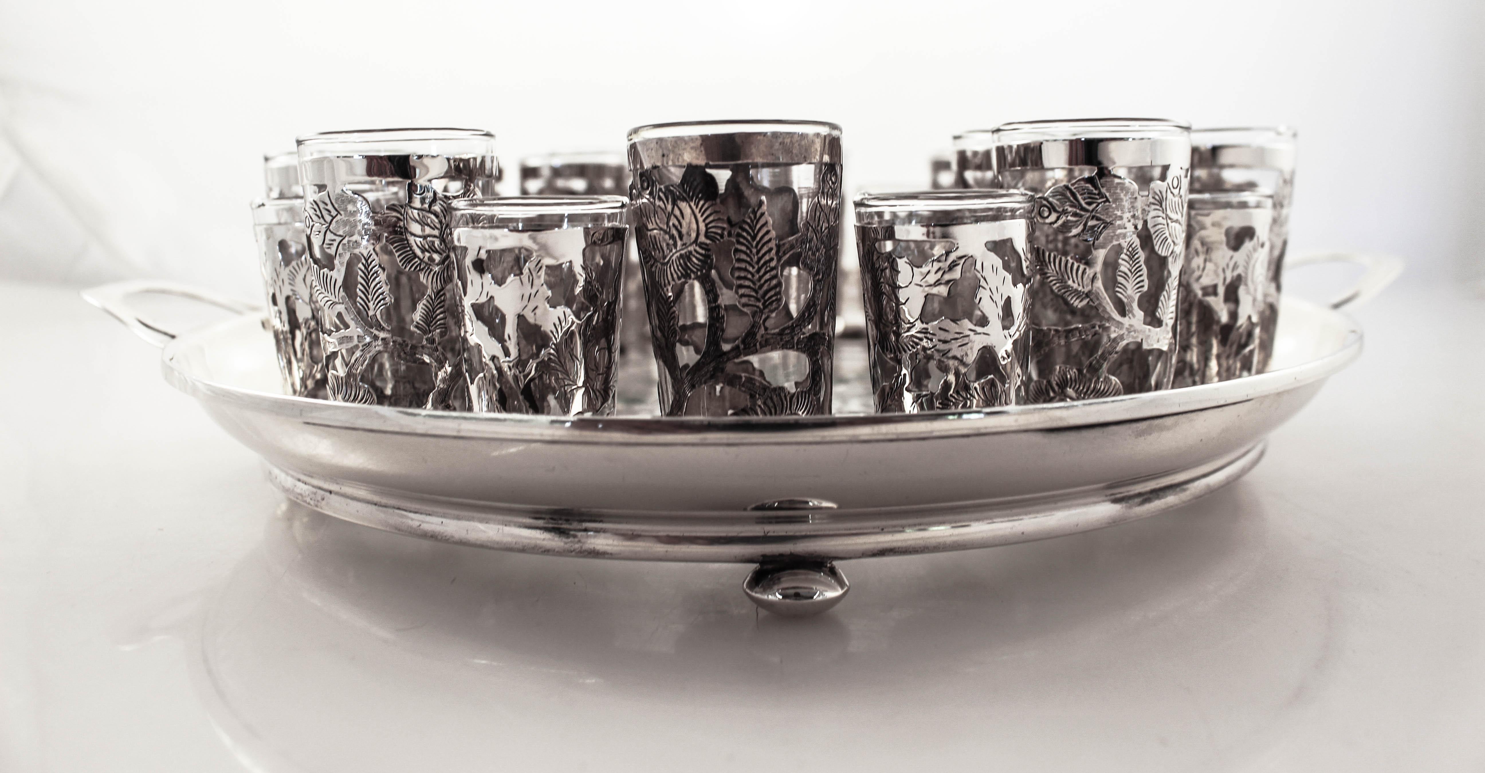 We are delighted to offer this large sterling silver liquor set that includes 24 glasses (12 larger and 12 smaller ones) and a tray. Each glass has a floral latticework overlay design. The glass portion is removable so it’s super easy to wash— even