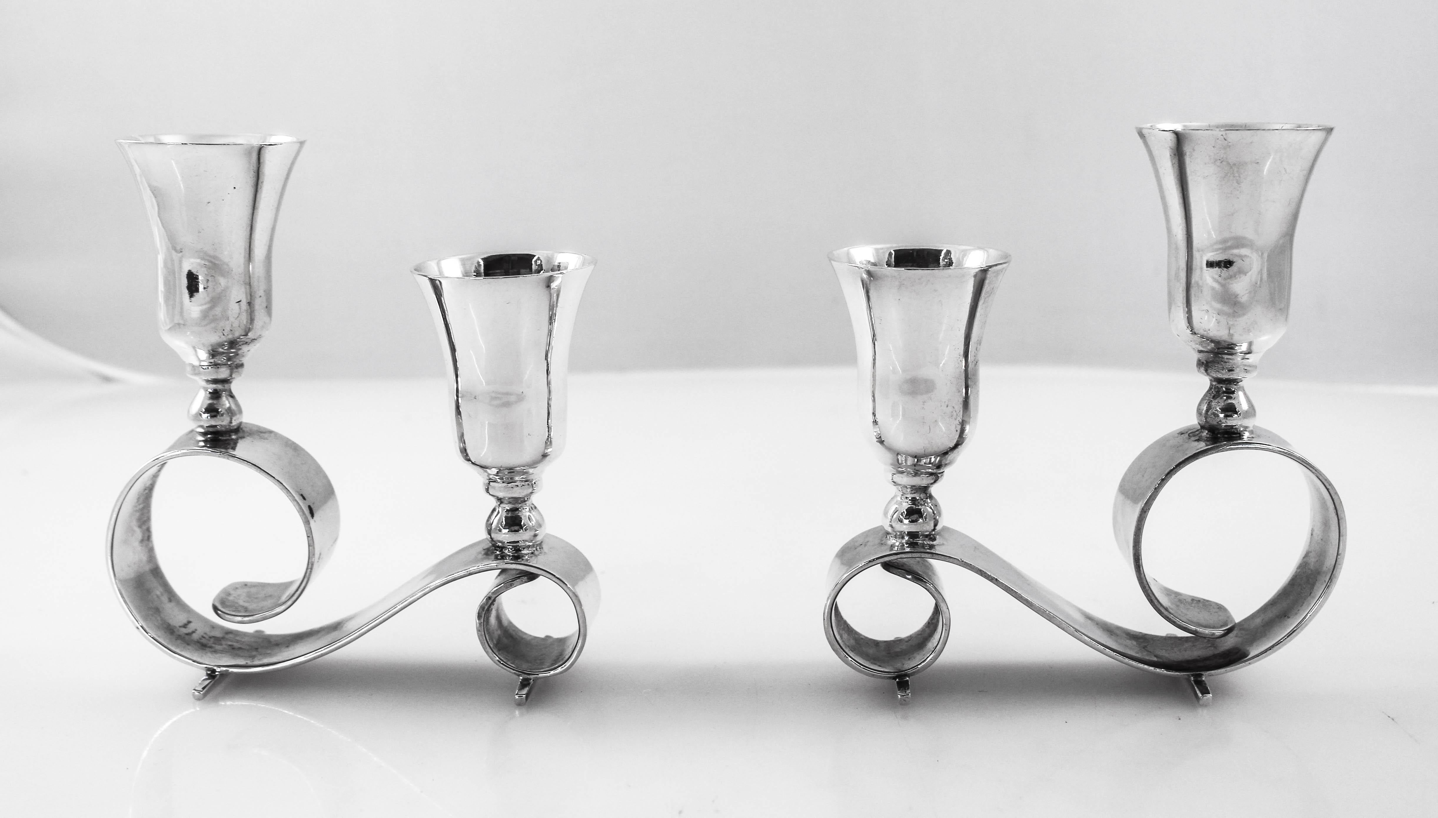 A pair of sterling silver two-branch midcentury candelabras. These candelabras are very unique in their shape and design. Standing on a single curved piece of silver, there is a difference of an inch between the upper and lower bobeche. This allows