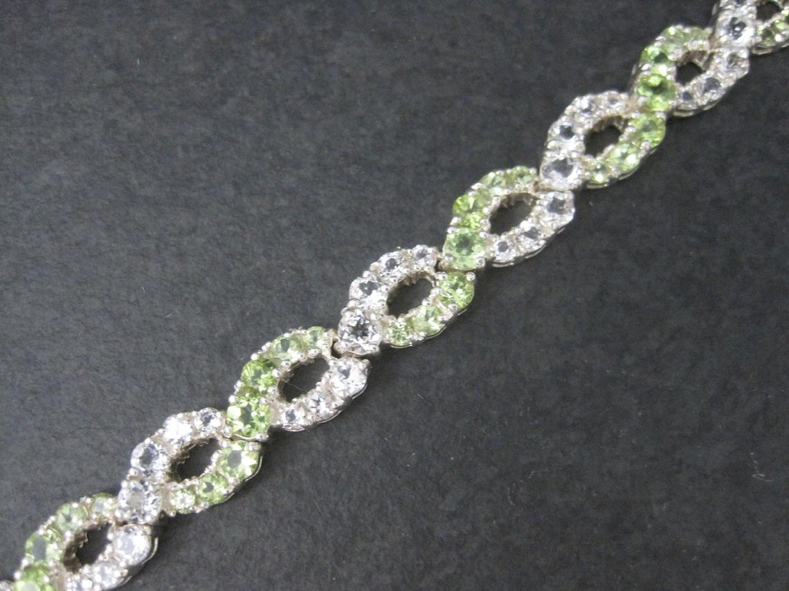 This stunning estate bracelet is sterling silver.
It features an estimated 7 cwt in peridots and 7ctw in white topaz.

Measurements: 3/8 of an inch wide - 7 1/4 wearable inches
Weight: 21.9 grams

Marks: 925, Thailand

Condition: Excellent