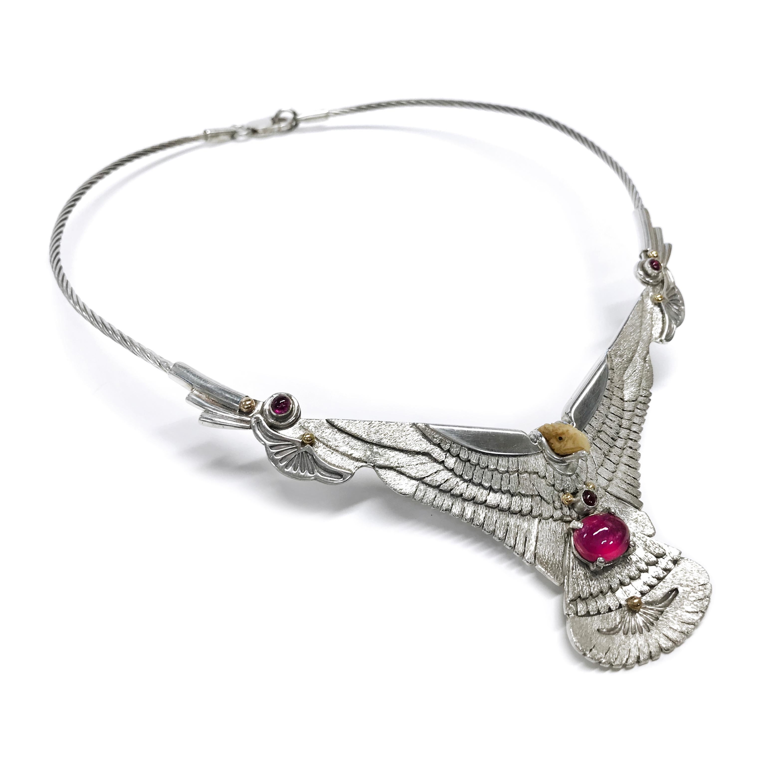 Handcrafted from a Sterling Silver sheet by jewelry maker, Ray Winner. The choker necklace consists of a silver eagle with outspread wings. The eagle head is made of carved bone and there is one prong-set oval Ruby cabochon and three round