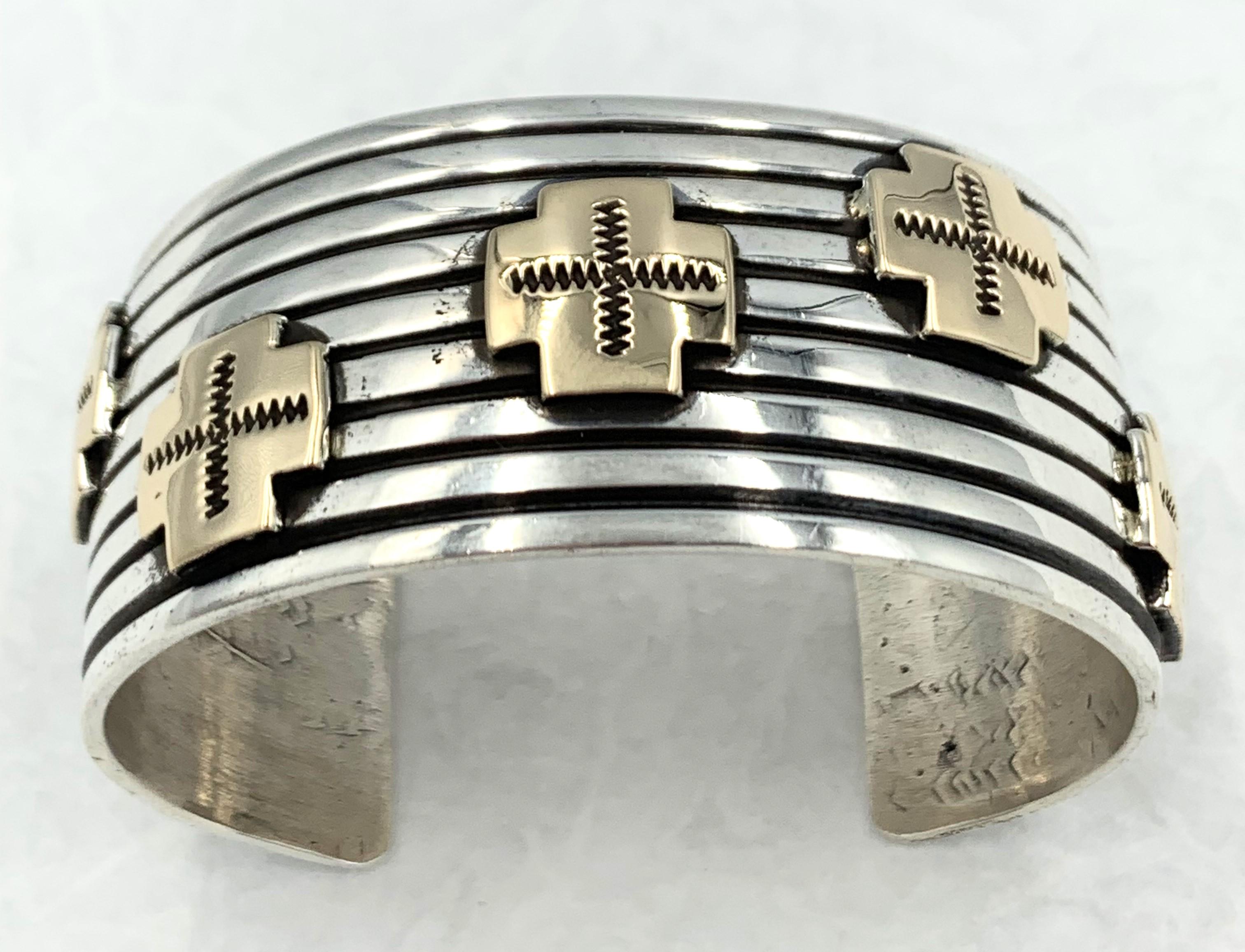 Dramatic, deeply grooved and ribbed cuff bracelet by Navajo silversmith Albert Jake. This smooth rounded 1 1/2” sterling silver bracelet has been deeply stamped with eight horizontal grooved bands showcasing five 14k gold crosses. The deep stampwork