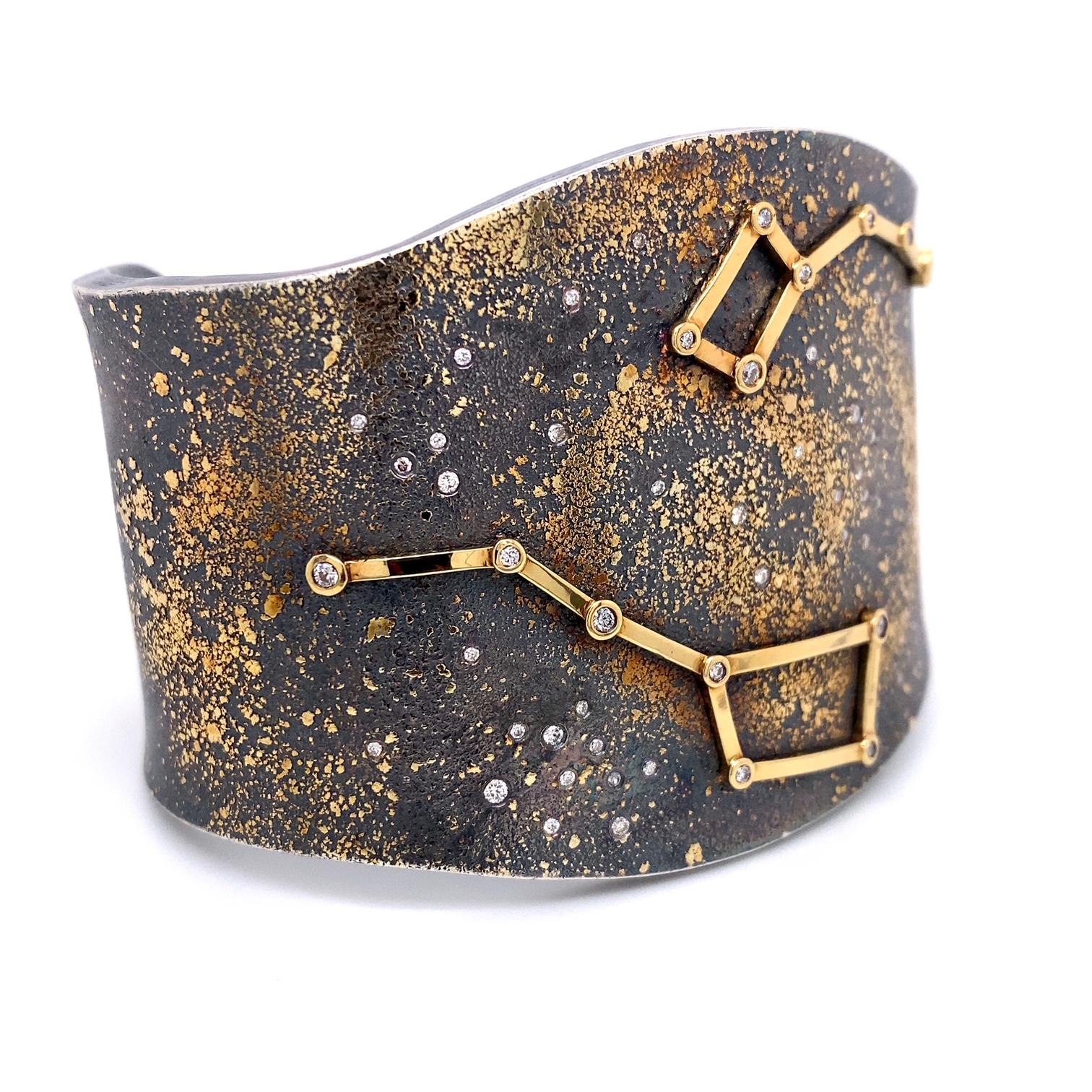 An oxidized sterling silver cuff bracelet with 18k yellow gold Ursa Major and Ursa Minor constellations, a 24k gold Milky Way Galaxy in the background, and set with 0.47 total carat weight round full cut white diamonds F color VS clarity. Designed