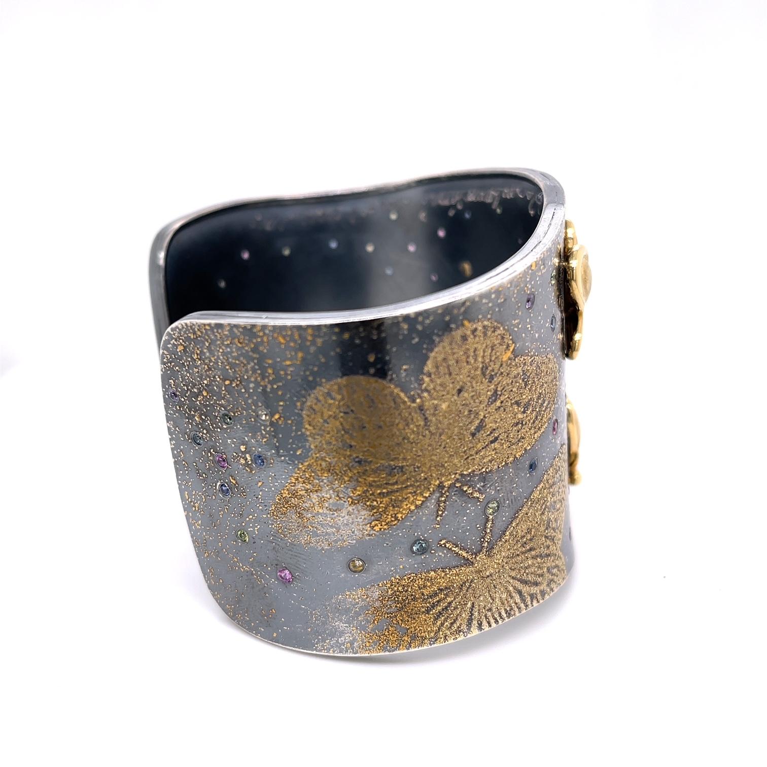 An oxidized sterling silver cuff with 24k yellow gold fairy dust butterflies and 18k yellow gold sculptural butterflies. Set with 1.24 carats of multi-colored sapphire, titled 