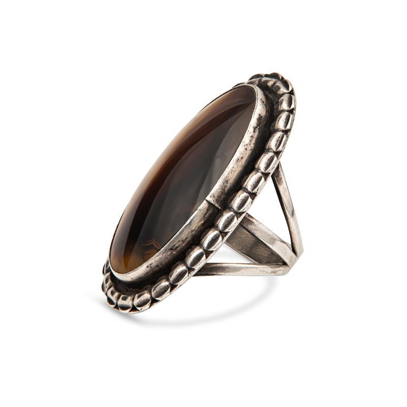 This sterling silver ring features a large elongated oval shaped agate accented by intricate silver work set on a triple shank. It is a size 6.5 but can be resized upon request. This ring at the longest point is approximately 1 5/8