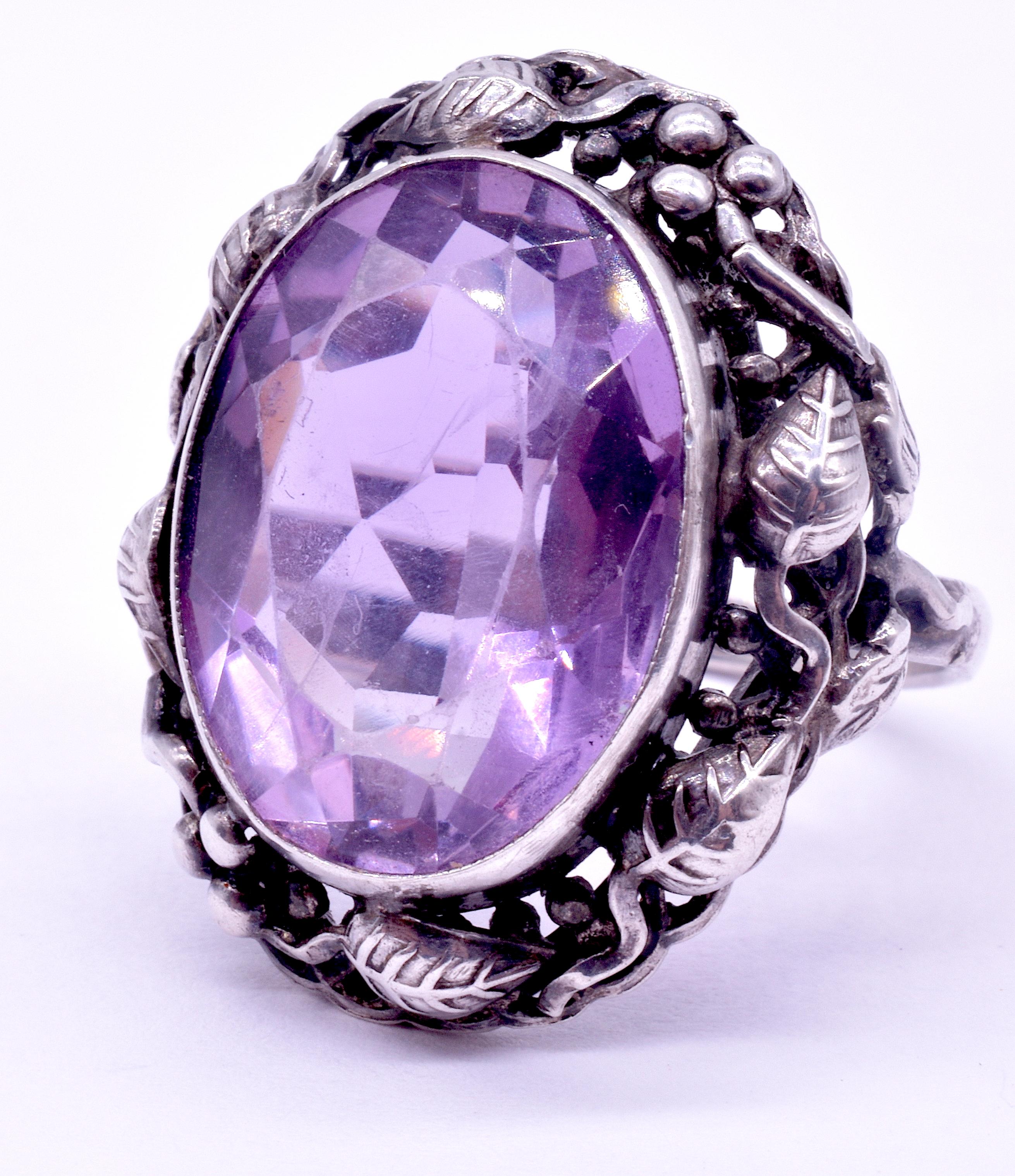 Lovely prominent amethyst ring in the Arts and Crafts style. The large and lovely amethyst is bordered by a silver border of well defined leaves - even the veining of the leaves can be seen, along with the round fruit of the branch. Theory behind