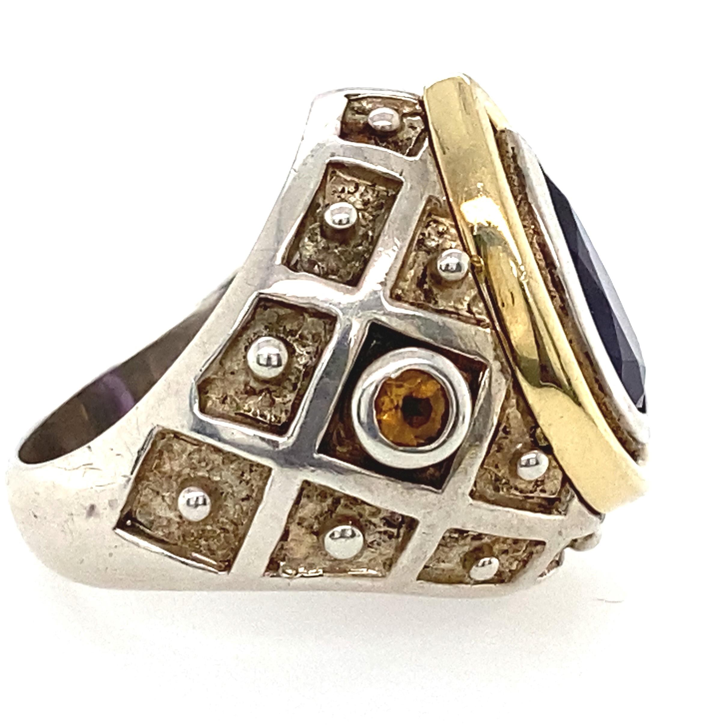 This is a sterling silver ring with 18kt  yellow gold accents hand made by renowned designer Mitchell Peck. The ring contains one center pear shaped 2.30 carat deep purple amethyst  bezel set in the center with two bezel set citrines on either side.