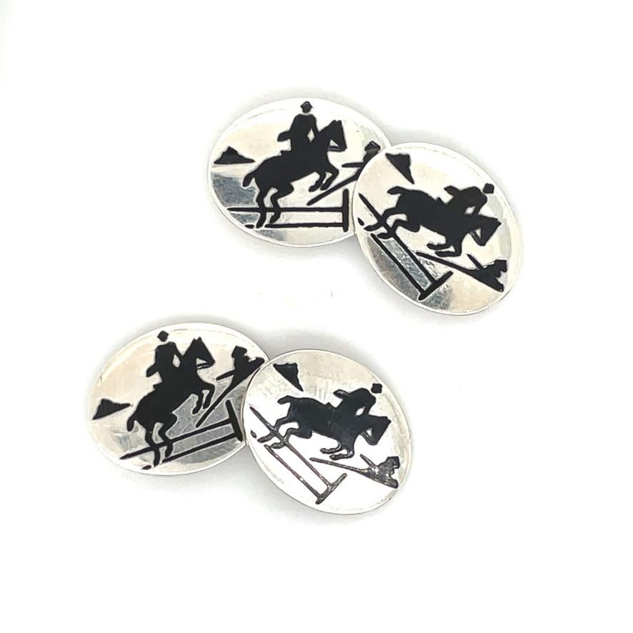 Ovale doppelseitige Manschettenknöpfe aus Sterlingsilber mit einer Szene eines über einen Zaun springenden Pferdes in schwarzer, handgemalter Emaille. Amerikanisch.  Um 1915.  3/4 x 1/2
