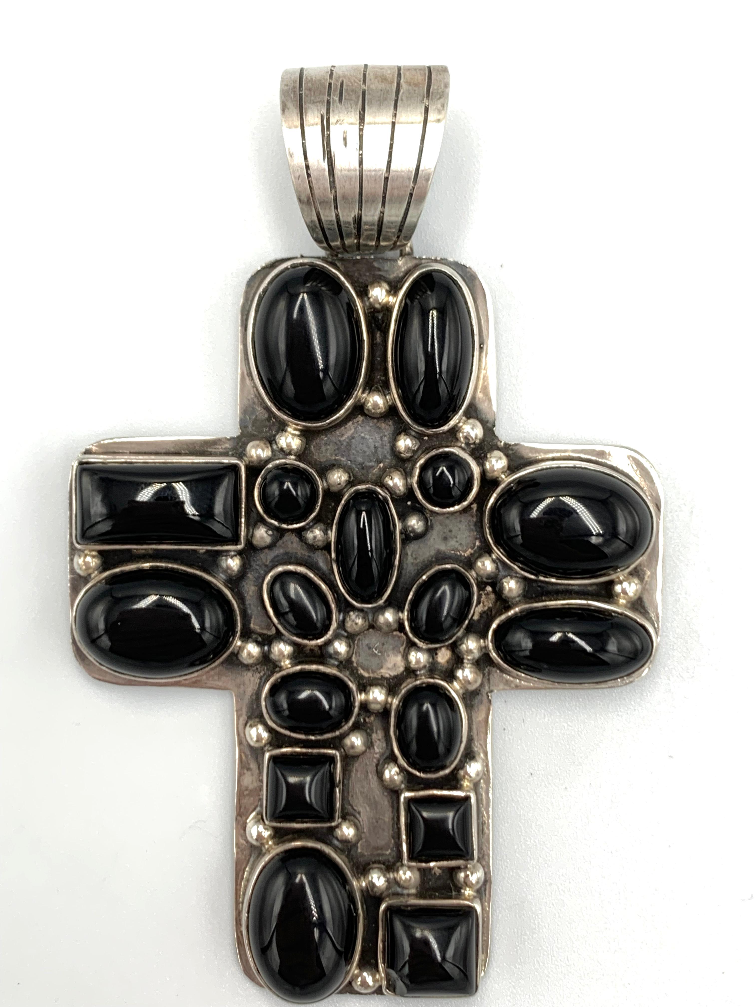 Ce pendentif en forme de croix en argent sterling de l'orfèvre de Santa Fe Dan Dodson met en valeur dix-sept cabochons d'onyx, chacun étant serti dans un chaton d'argent détaillé et rehaussé de multiples gouttes de pluie en argent sterling. La croix
