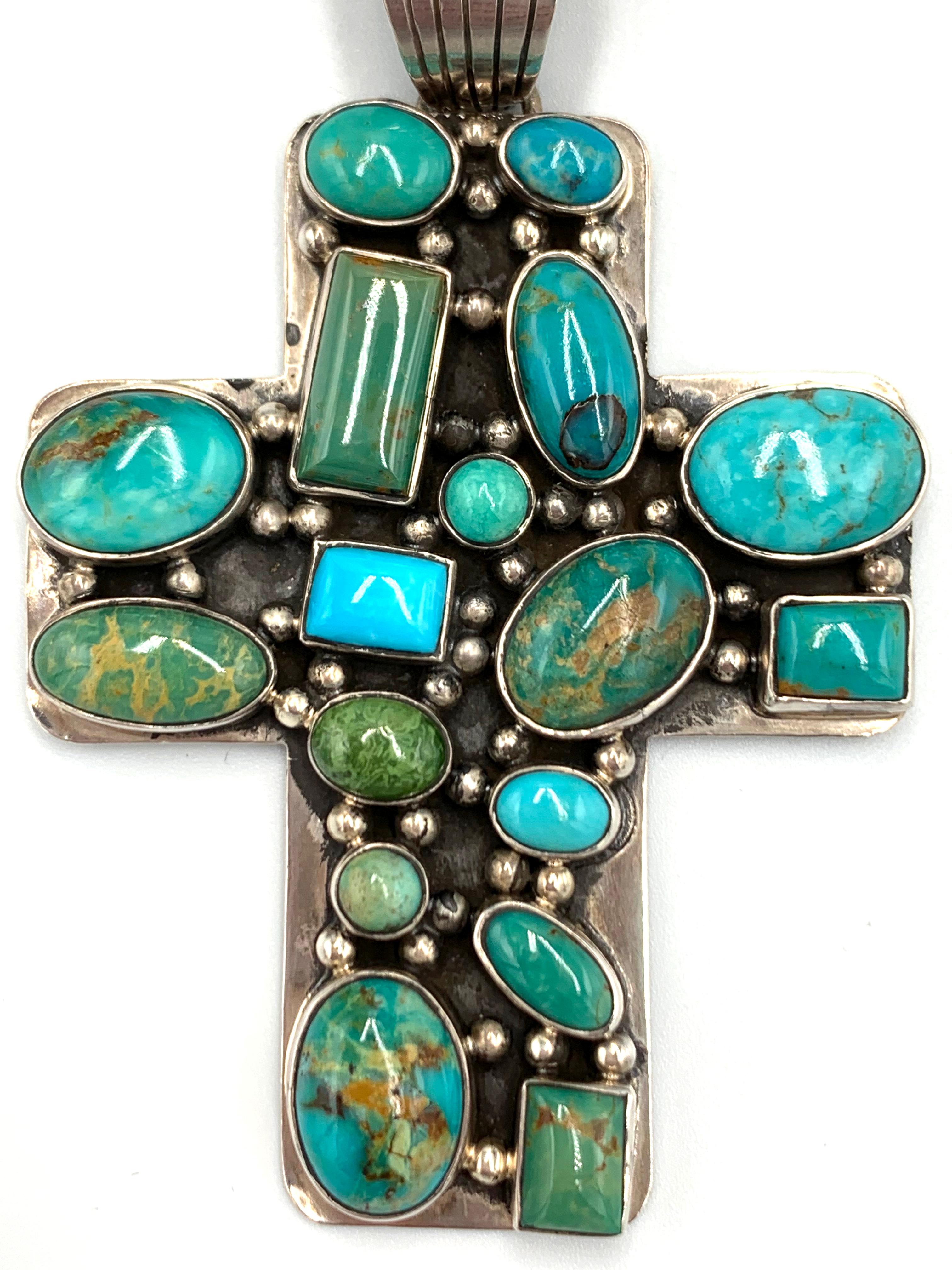 Ce pendentif en forme de croix en argent sterling de l'orfèvre de Santa Fe Dan Dodson présente dix-sept cabochons de turquoise provenant de différentes mines, rehaussés de multiples gouttes de pluie en argent sterling. La croix mesure 2 1/8