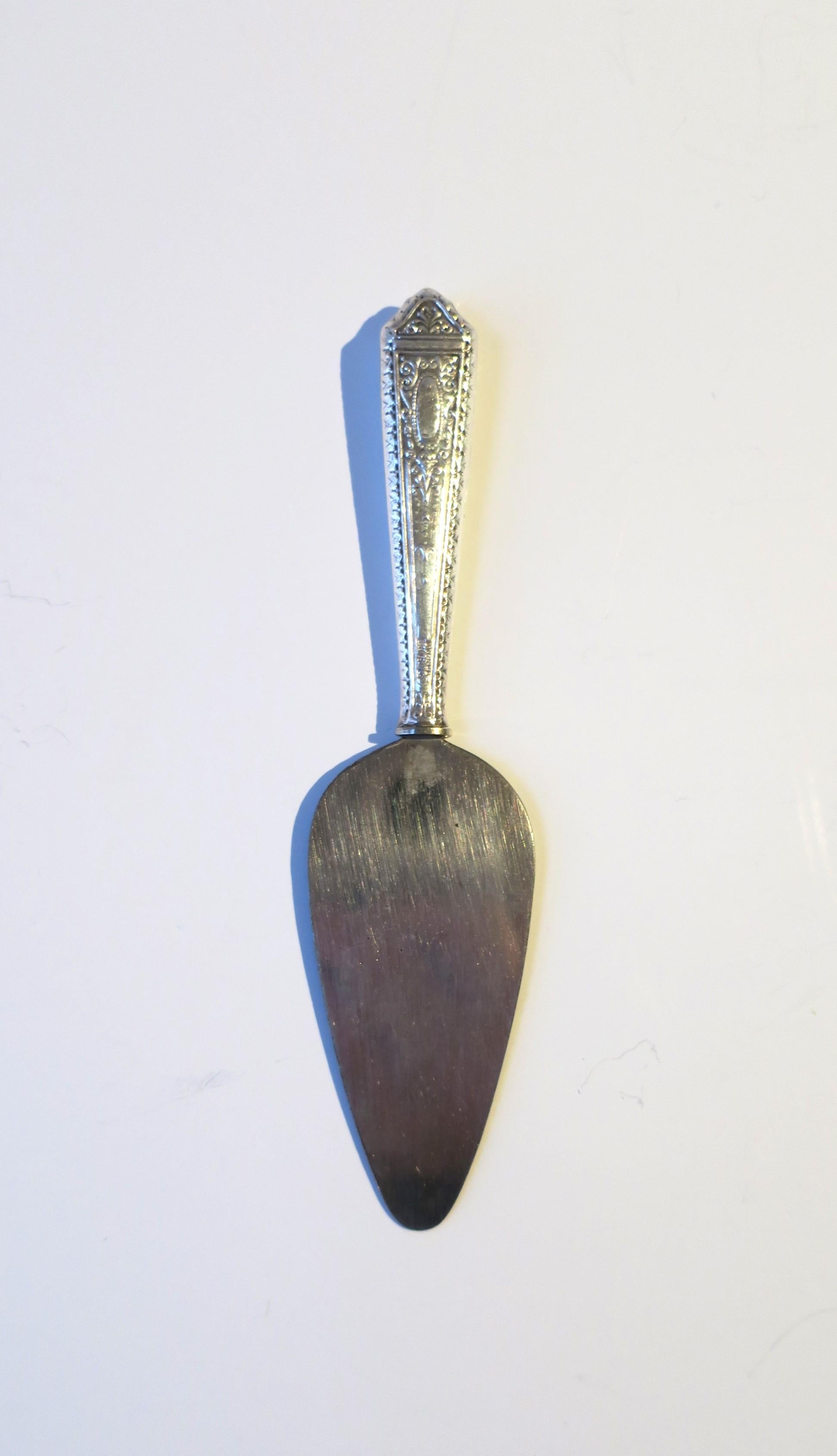A sterling silver appetizer spreader, circa early-20th century. Pieces' sterling silver handle has a repousse design of beads and scrolls, spreader/spatula in stainless steel. Handle is marked, on both sides. 'Sterling', 'Handle', shown in closeup