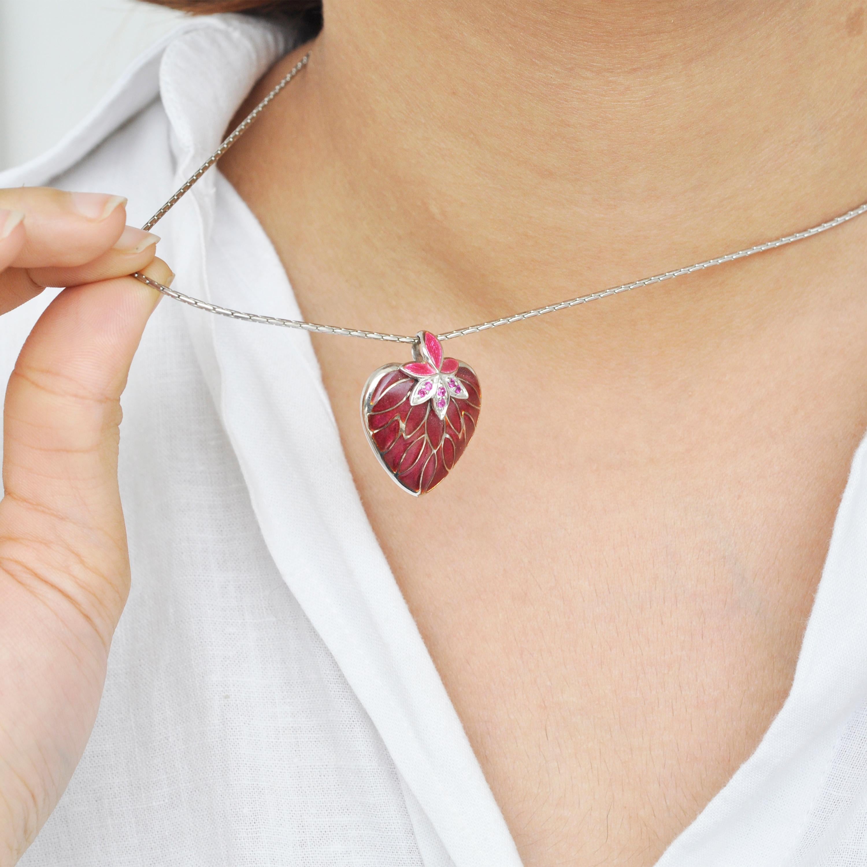 Ce magnifique pendentif Apple Red Heart en argent sterling, émaillé d'une plique-à-jour d'un rouge profond, est délicatement orné de tourmalines roses créées en laboratoire et disposées sur deux feuilles. Ce pendentif en forme de cœur a un  boucle