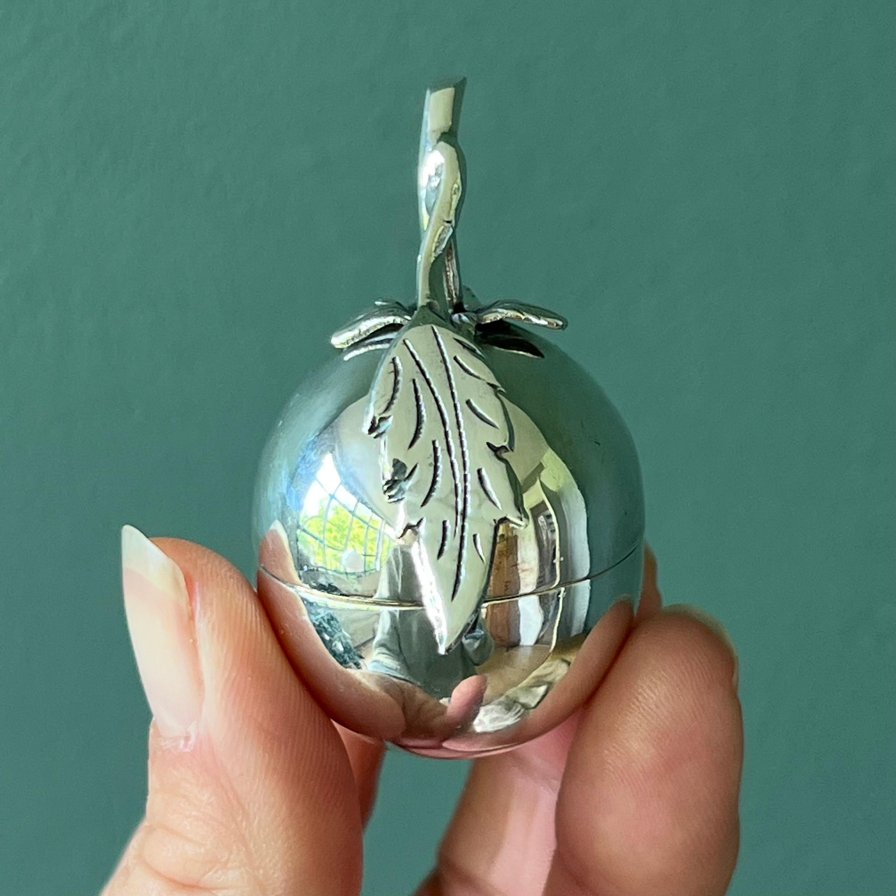 A charming and beautifully crafted sterling silver trinket box designed in the shape of an apple, this piece blends whimsical form with fine silversmithing. The smooth, polished body opens at the center, revealing a hollow interior ideal for holding