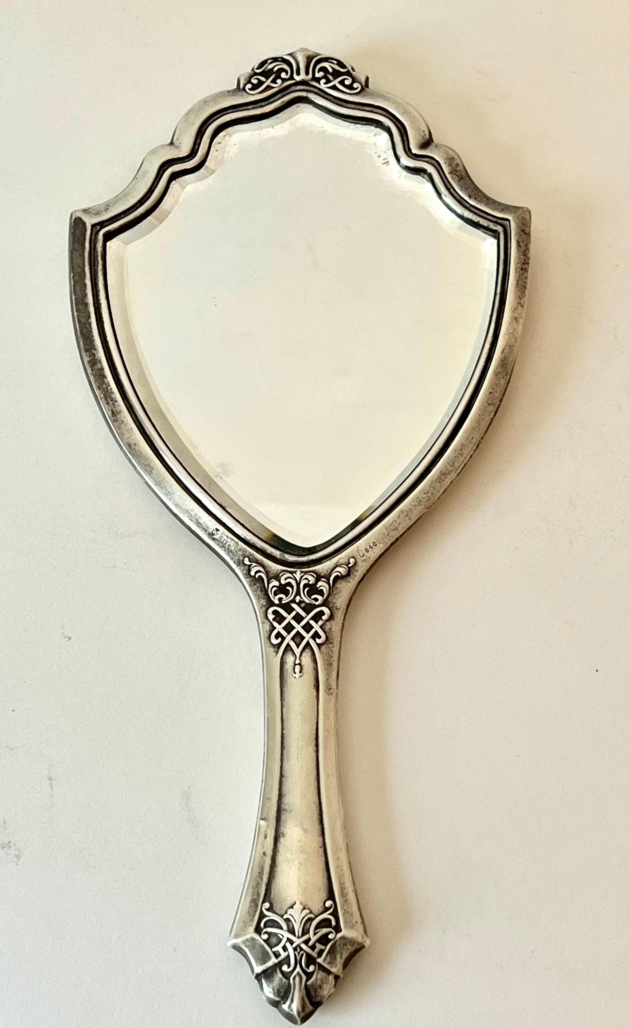 A beautifully designed Sterling Hand mirror with Art Nouveau design.  The patination is wonderful with some tarnish and marred areas due to age.   a compliment to any vanity or dressing area.   

The mirror is beveled enhancing the design -