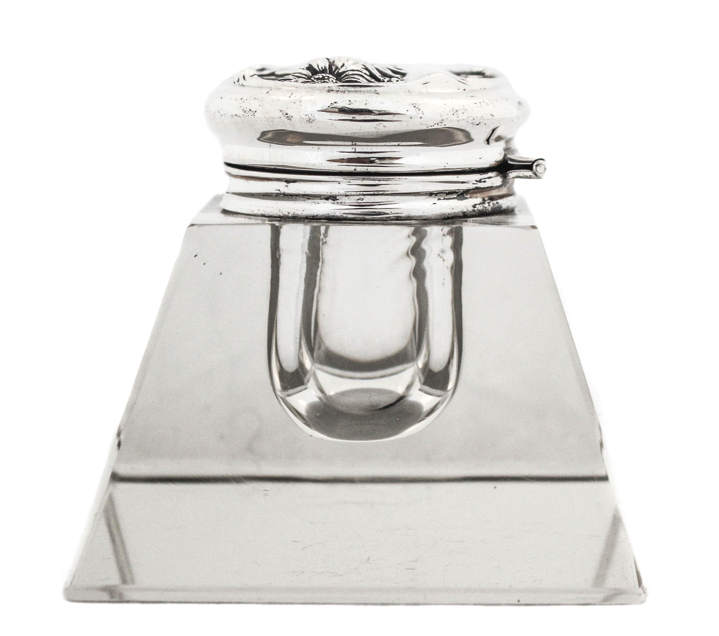 This sterling silver inkwell conjures memories of a time when letter writing was an art and people waited for letters from loved ones with anticipation. The lid has an Art Nouveau motif and lifts upwards. The base is square and has a flat bottom.