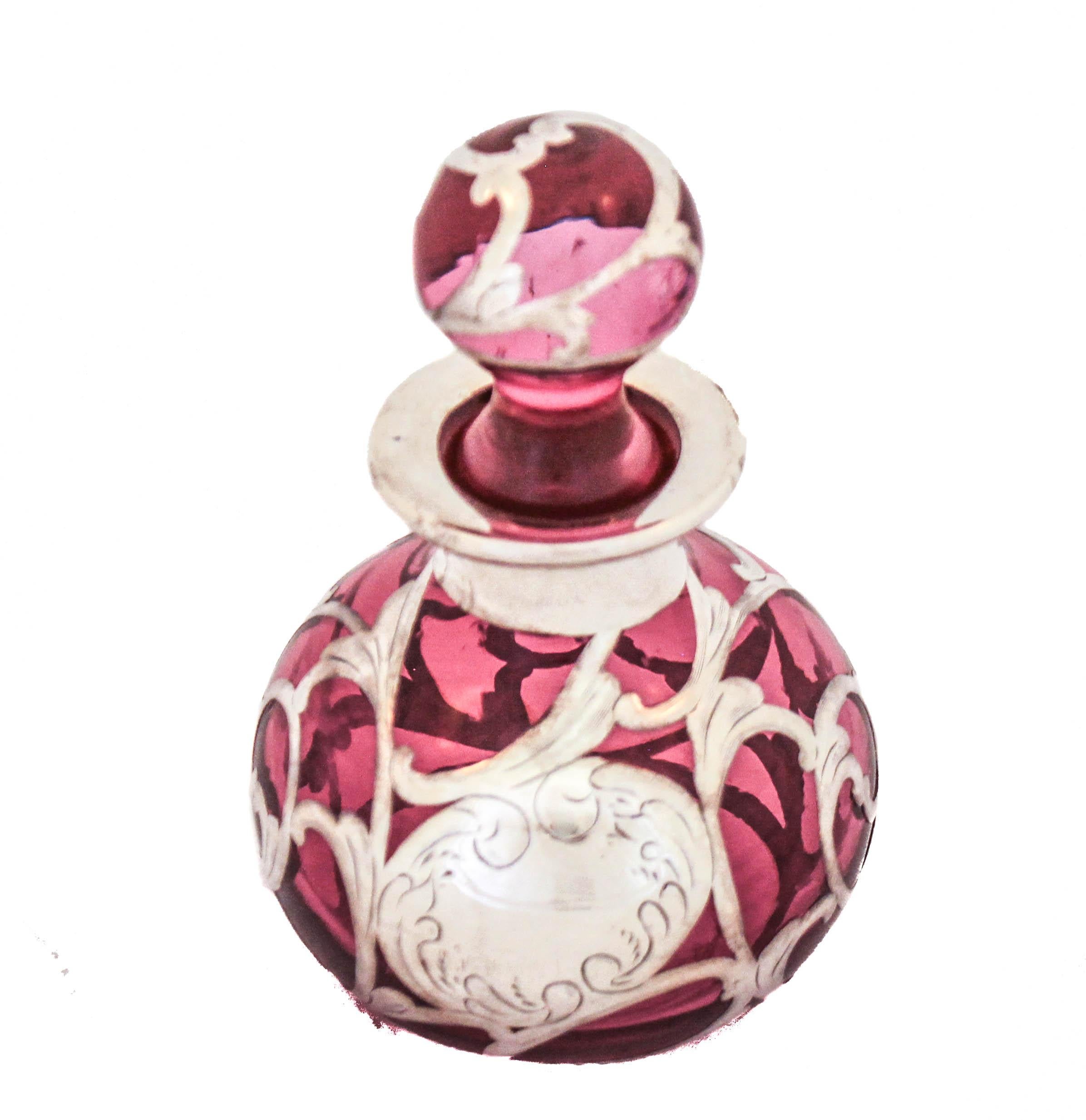 Being offered is a sterling silver Art Nouveau overlay perfume bottle.  This bottle has cranberry-red colored glass with silver overlay of swirls, flowers and leaves motif all around.  Unlike most overlay glass that has a dark red color this one is